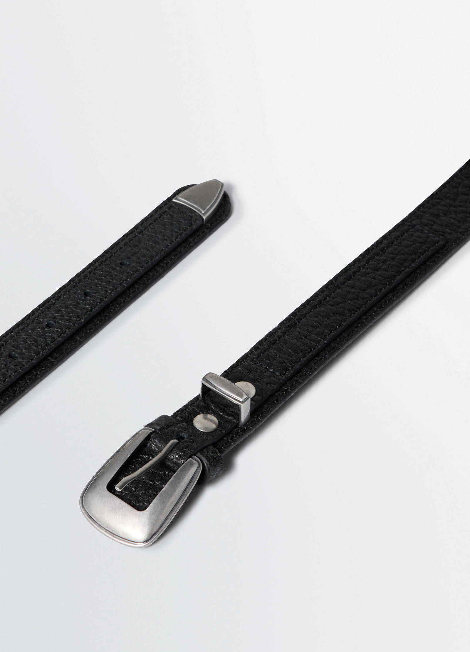 Minimal western belt in grained leather, product shot, angled close-up silver buckle accent