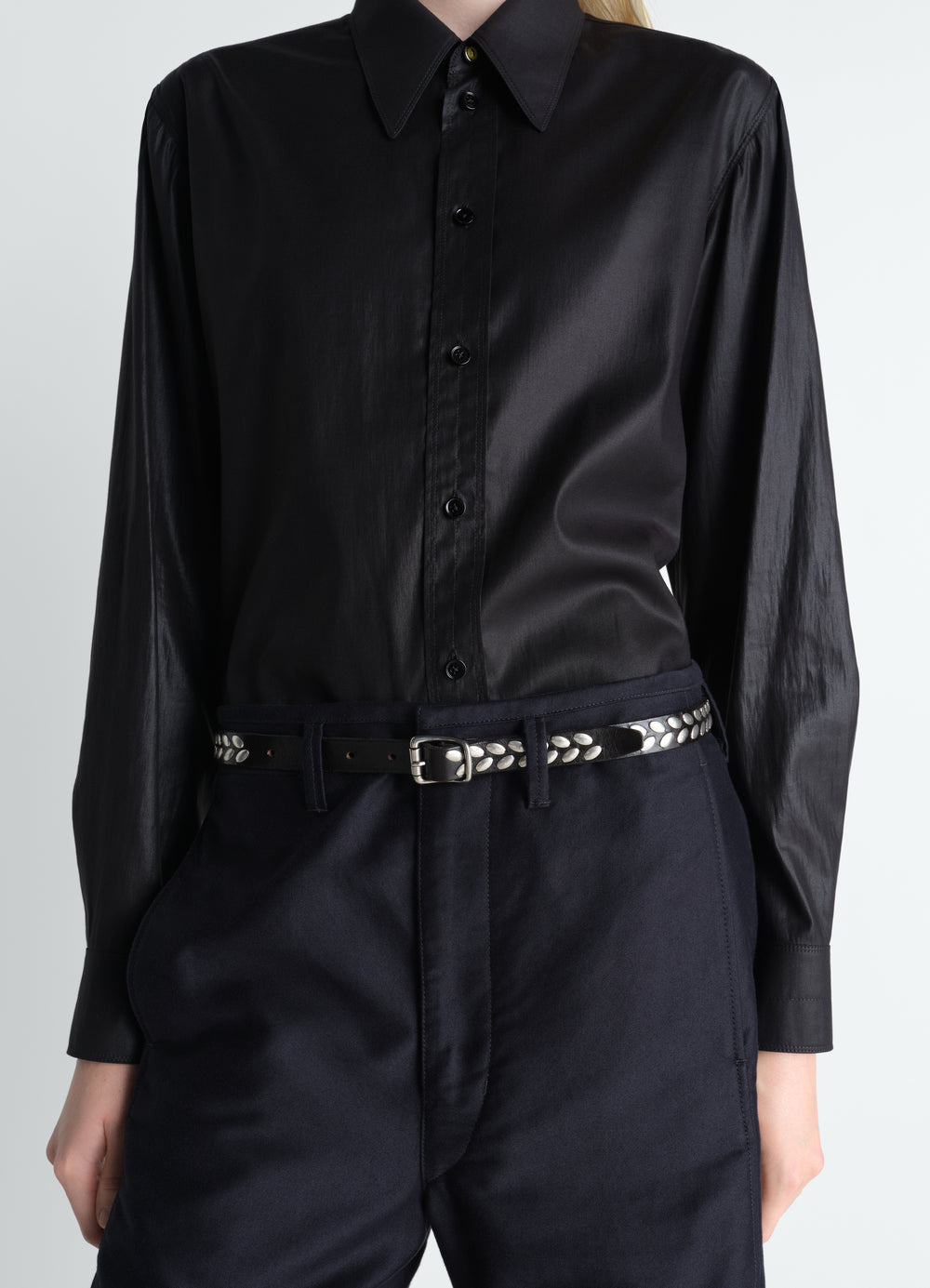 Almond Stud black leather belt by LEMAIRE worn by model with black button shirt and navy trousers front view