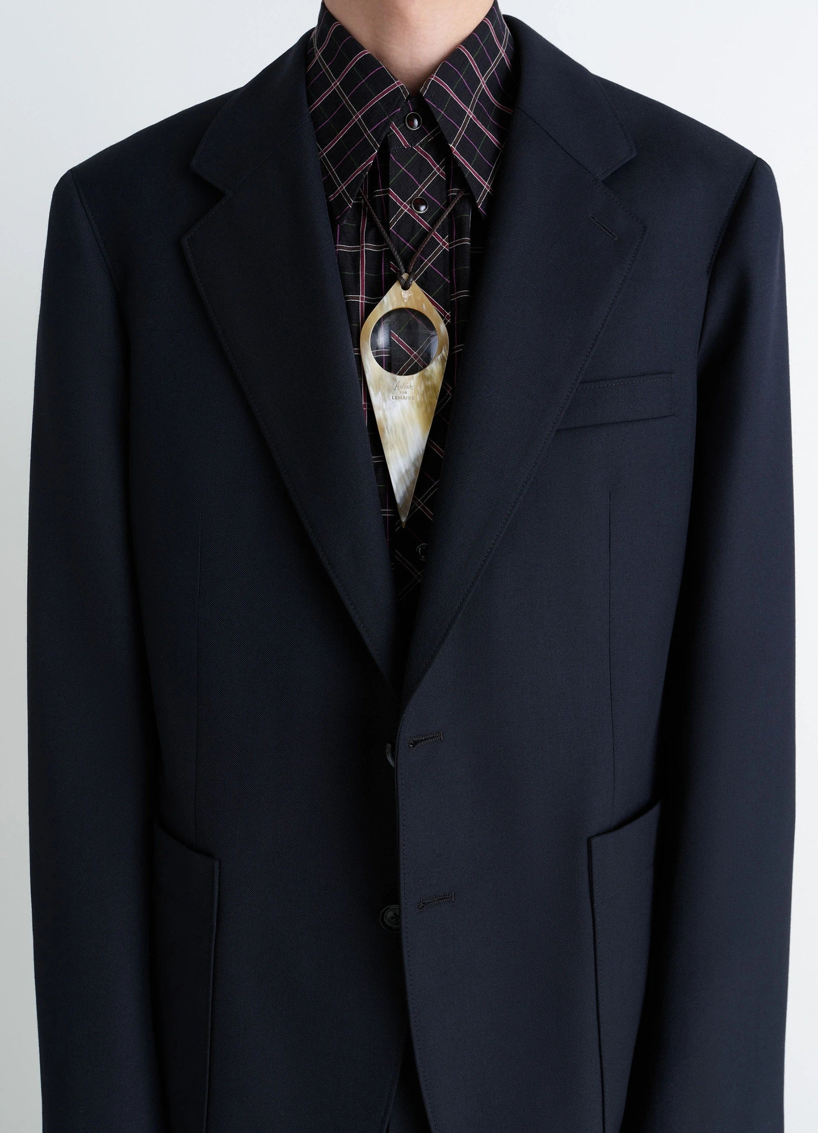 Aubock magnifying glass necklace in horn, model shot, mid-torso view worn over plaid shirt and blazer