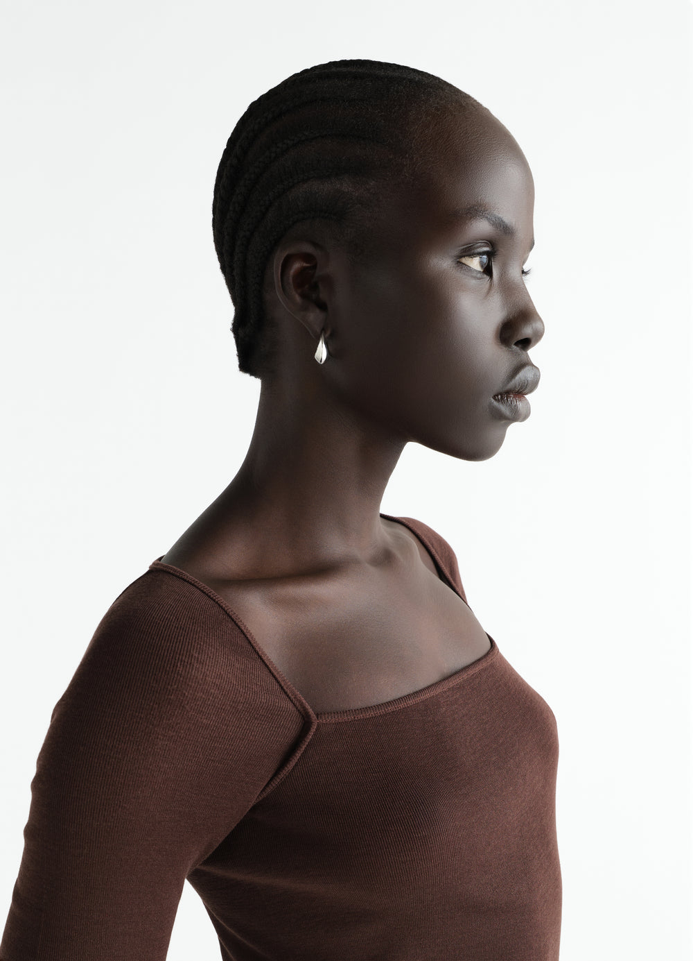 Curved Mini Drop In silver earrings by LEMAIRE worn by model with brown knit top side profile view