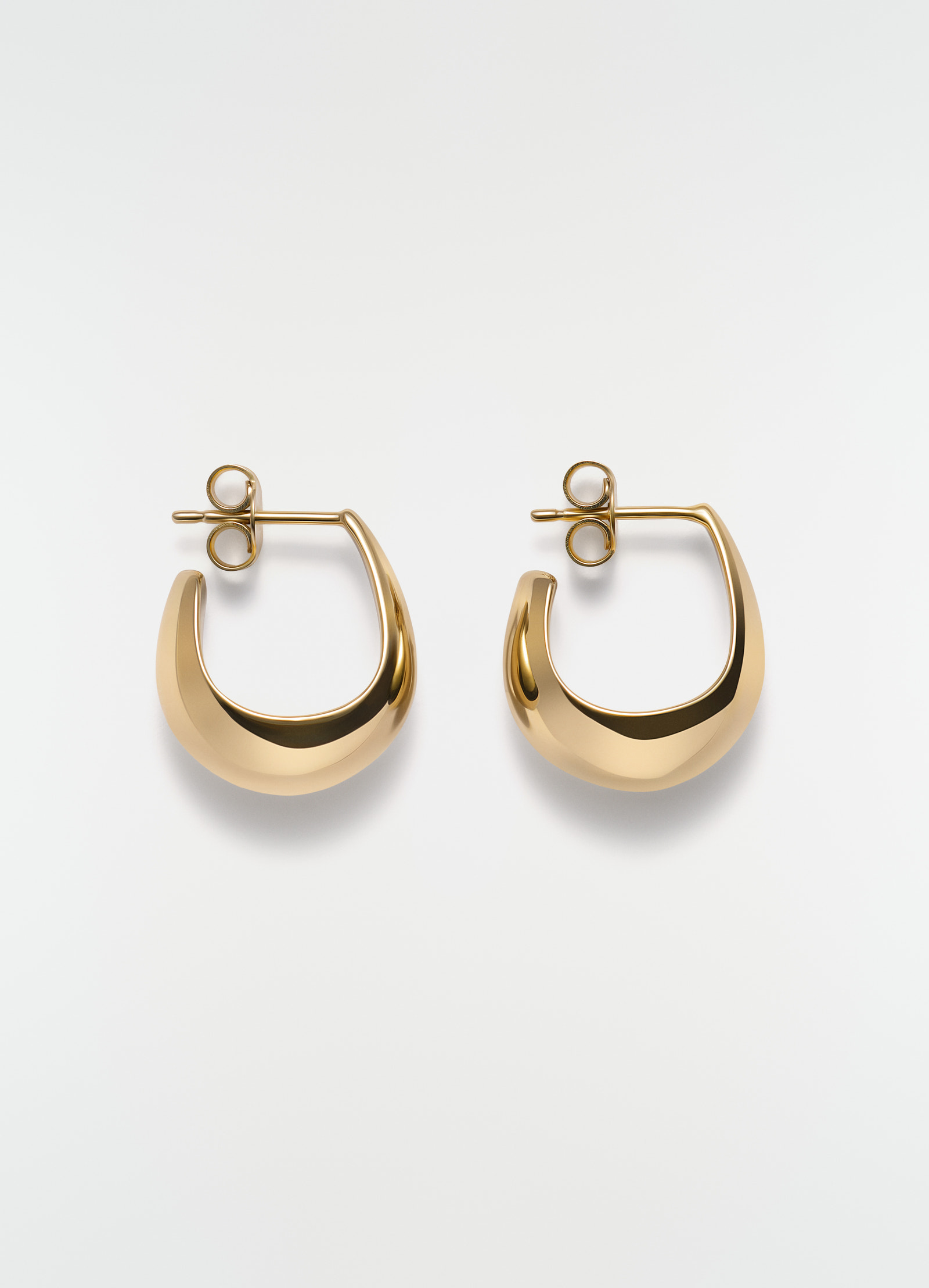 Curved mini drop vermeil gold earrings by lemaire flat lay on white background with post back closure