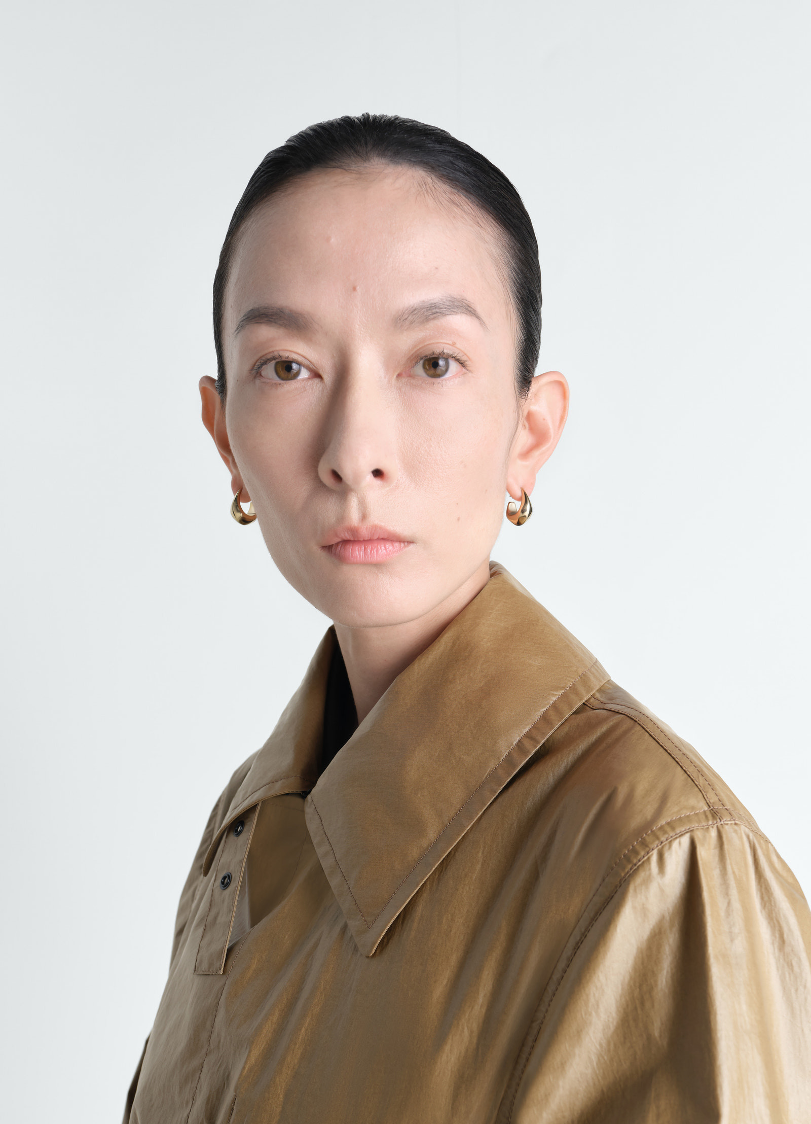 Curved mini drop gold vermeil earrings by lemaire worn by a model close-up on white background