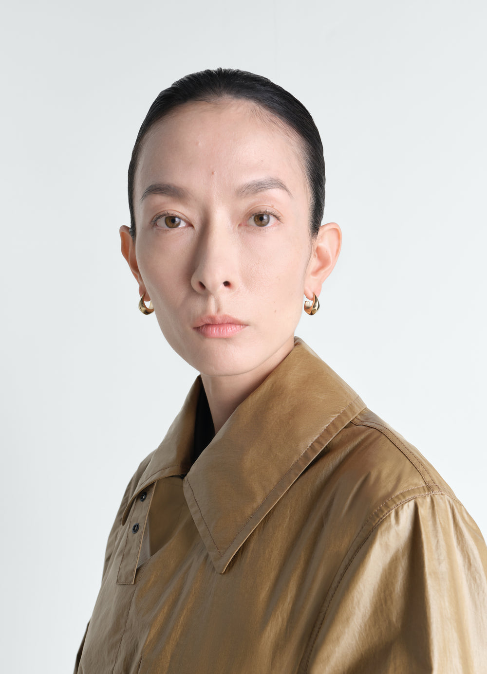 Curved mini drop gold vermeil earrings by LEMAIRE worn by a model close-up on white background