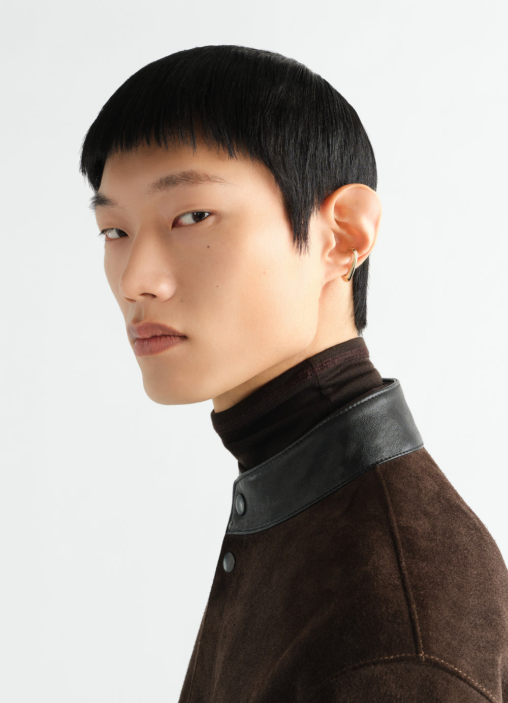 Long drop vermeil earcuff by LEMAIRE worn by model with black hair and brown suede jacket close-up side view