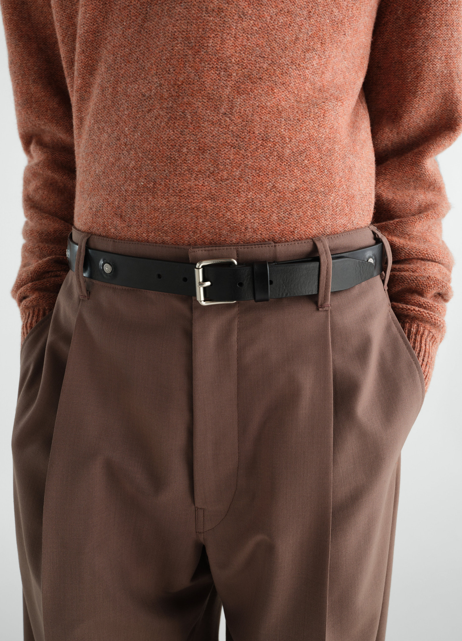 Marguerite black vegetable-tanned leather belt by lemaire worn by model with brown trousers and rust sweater