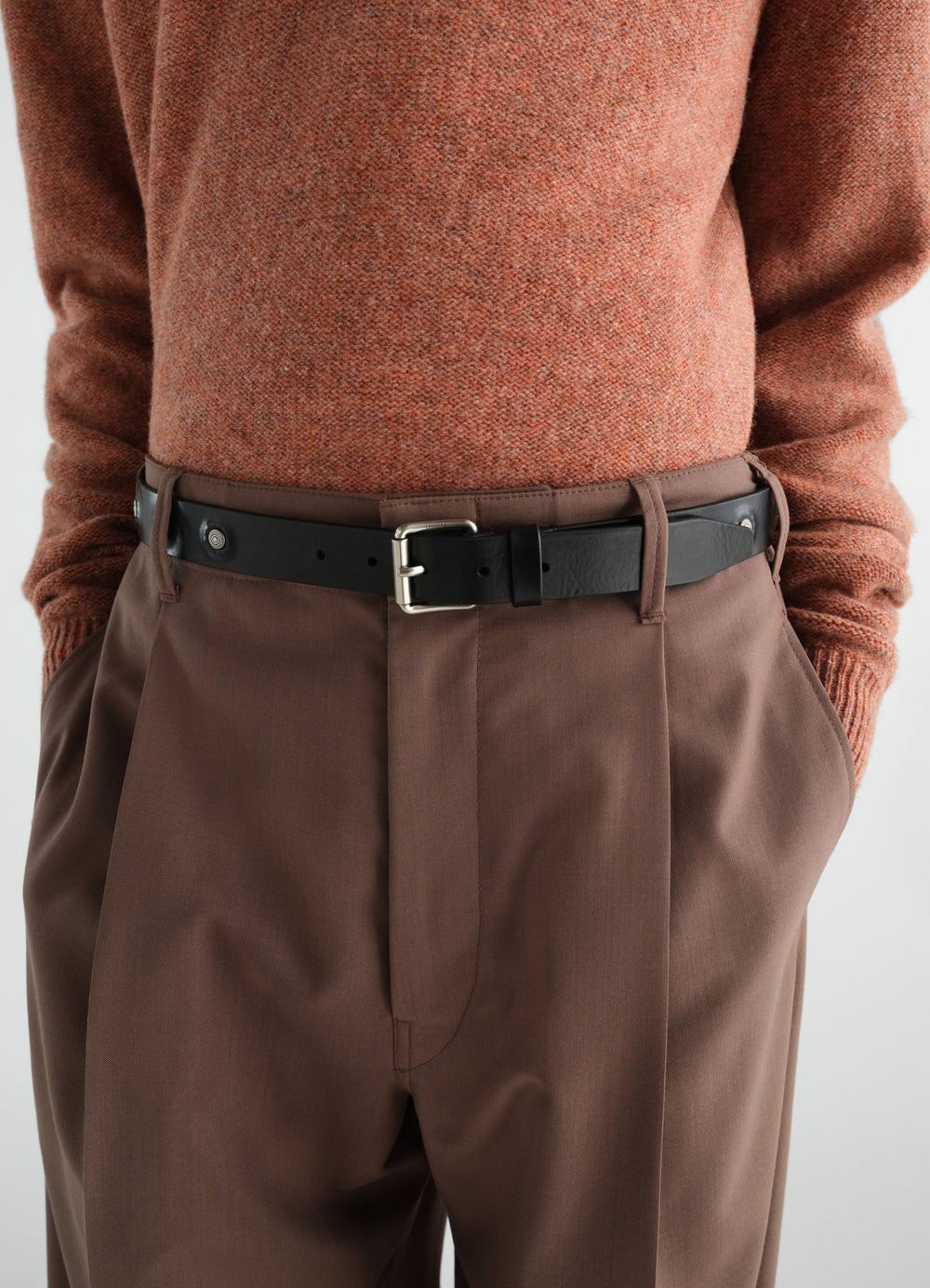 Marguerite black vegetable-tanned leather belt by LEMAIRE worn by model with brown trousers and rust sweater