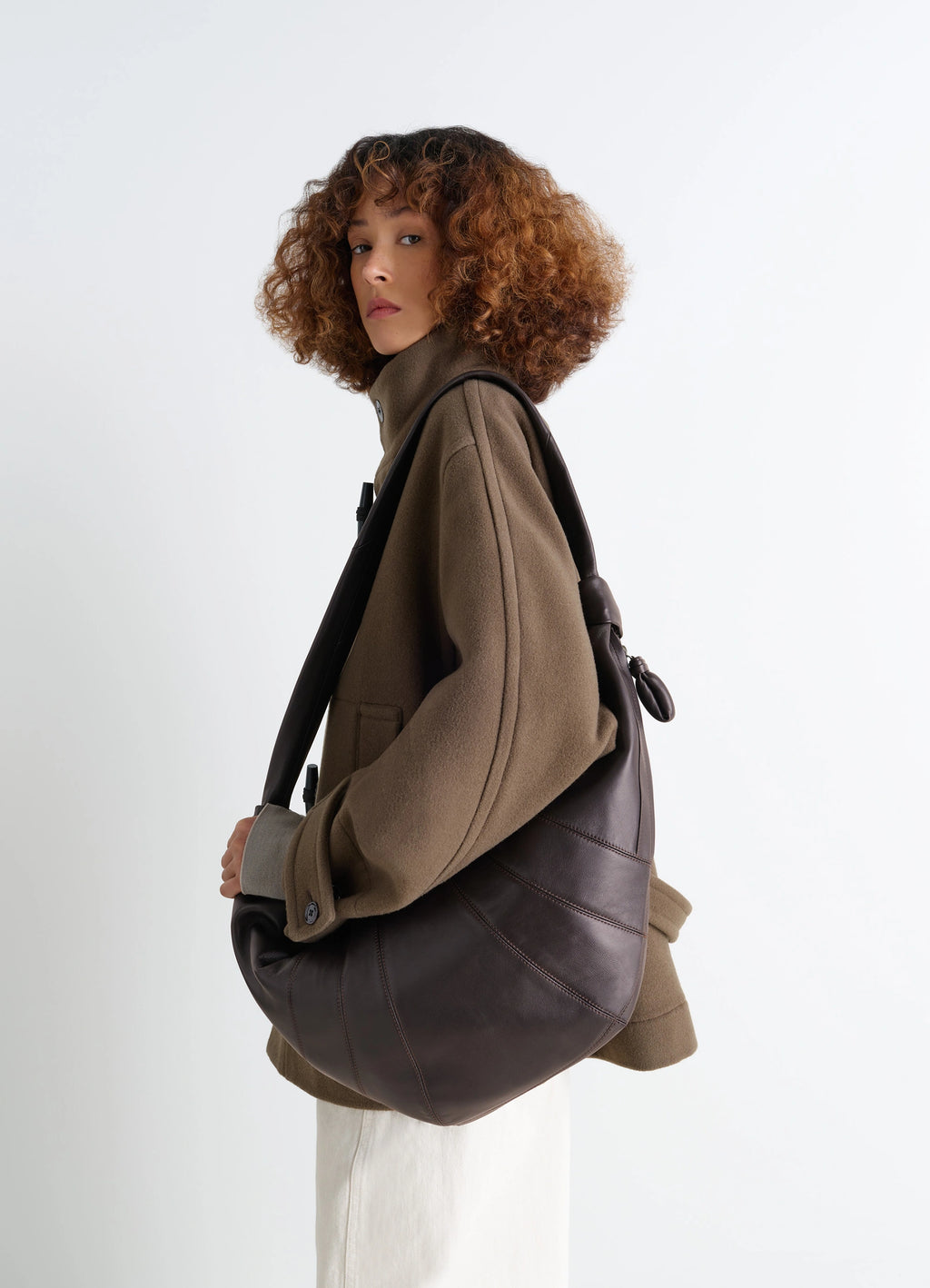 Lemaire Large Croissant Bag in Nappa Lamb Leather, model shot, over the shoulder view textural contrast with coat