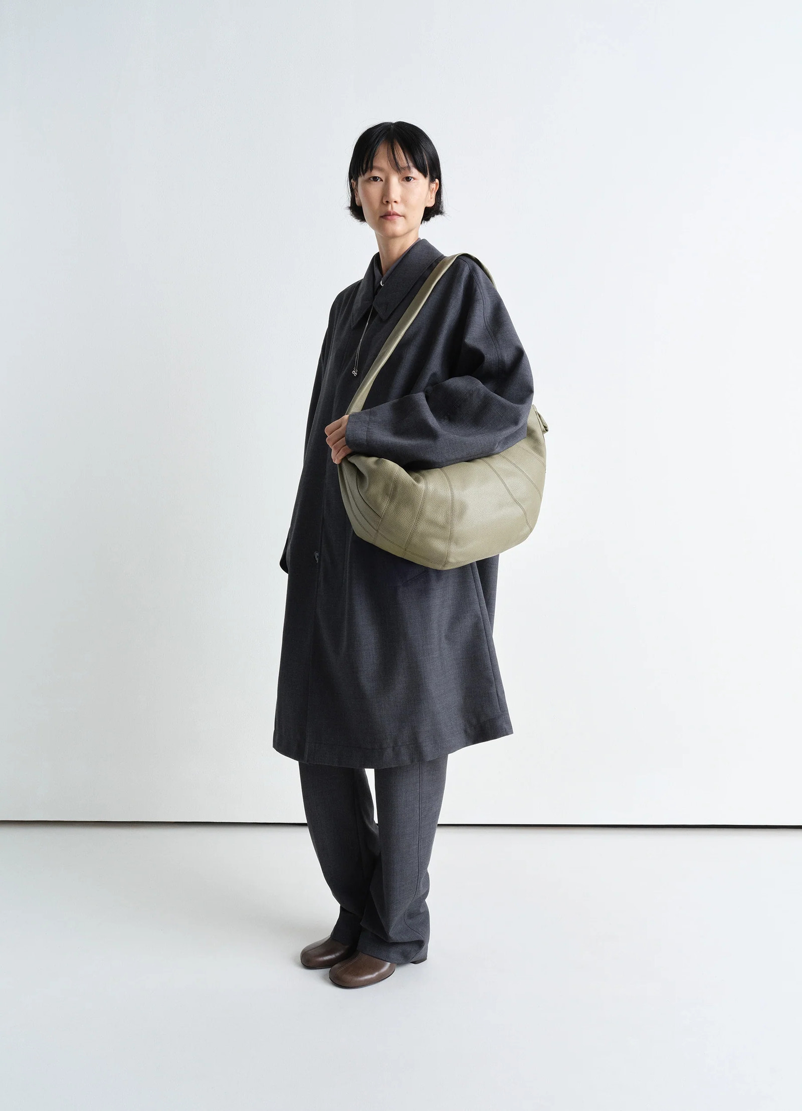 Lemaire large croissant bag in soft grained leather, model shot, three-quarter view worn crossbody overcoat