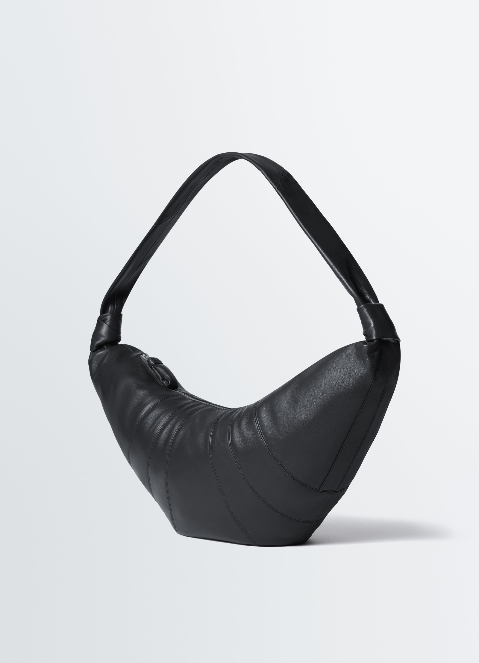 Large black leather croissant bag by lemaire studio shot on plain white background showing side and strap details