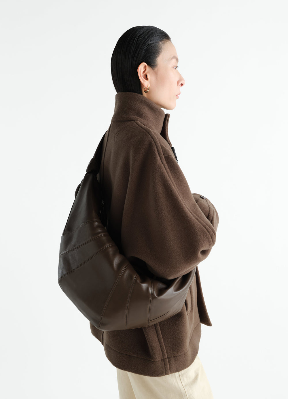 Large brown leather Croissant Bag by LEMAIRE worn by model side view with brown fleece jacket and cream pants