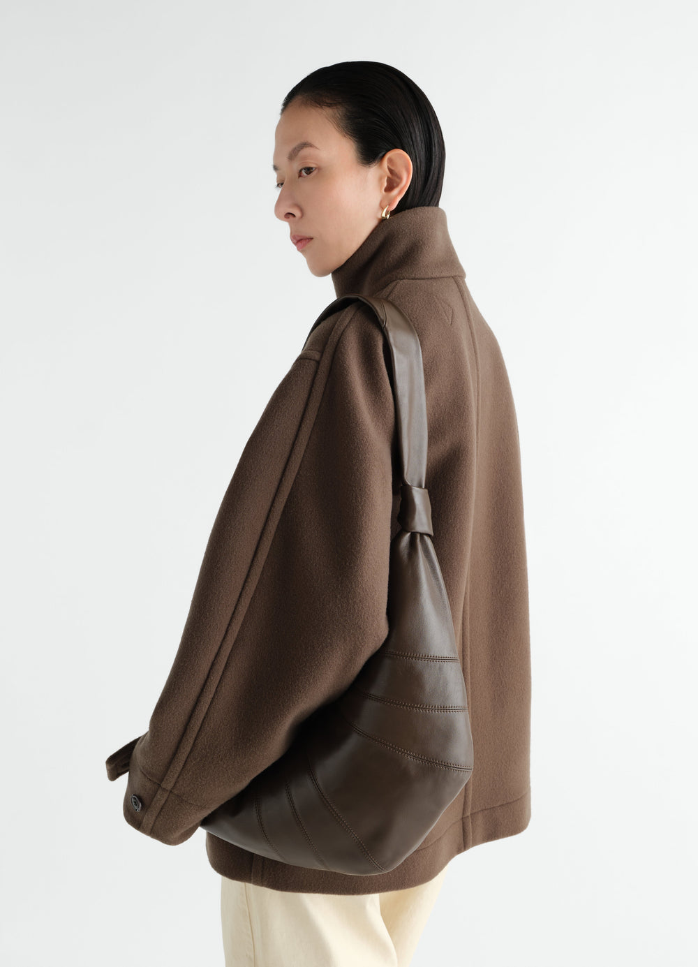 Medium Croissant bag in dark brown leather by LEMAIRE worn by a model side view against white background