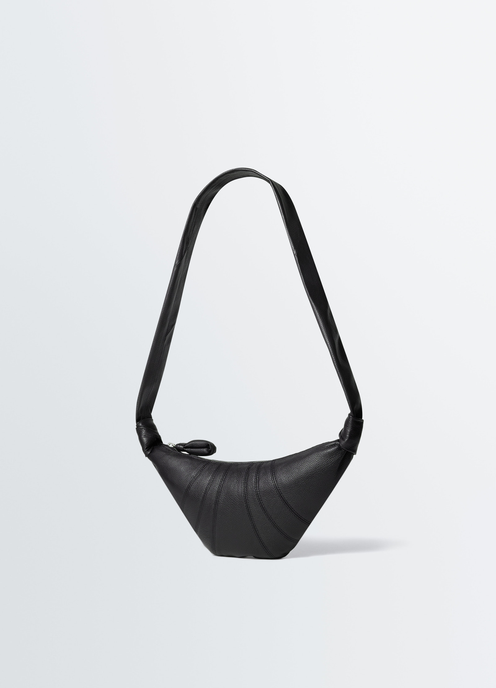Small black leather croissant bag with curved stitching lemaire front on plain white background