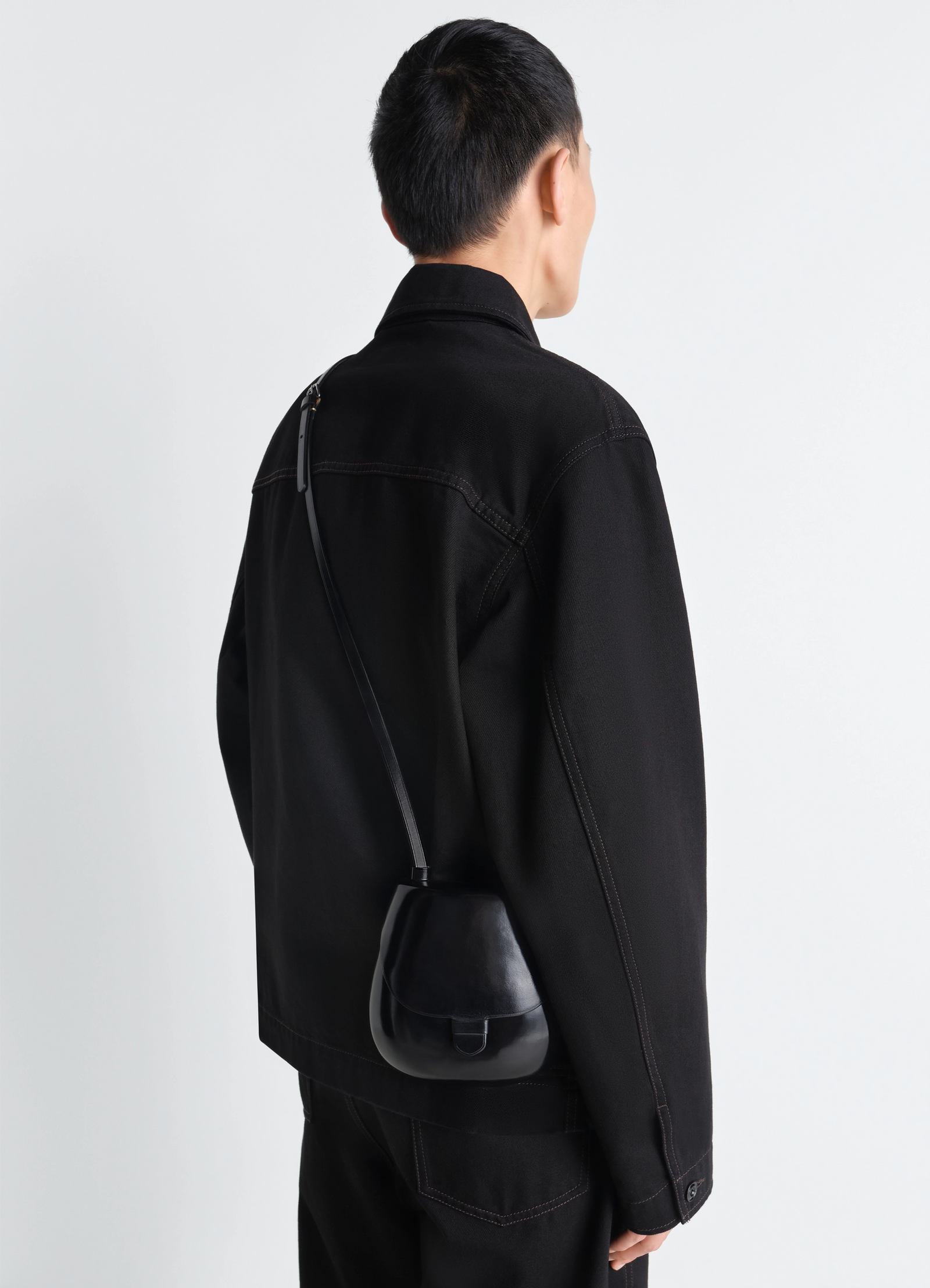 Il bussetto for lemaire small cartr in black molded vegetable-tanned leath, model shot, over-shoulder view crossbody with str