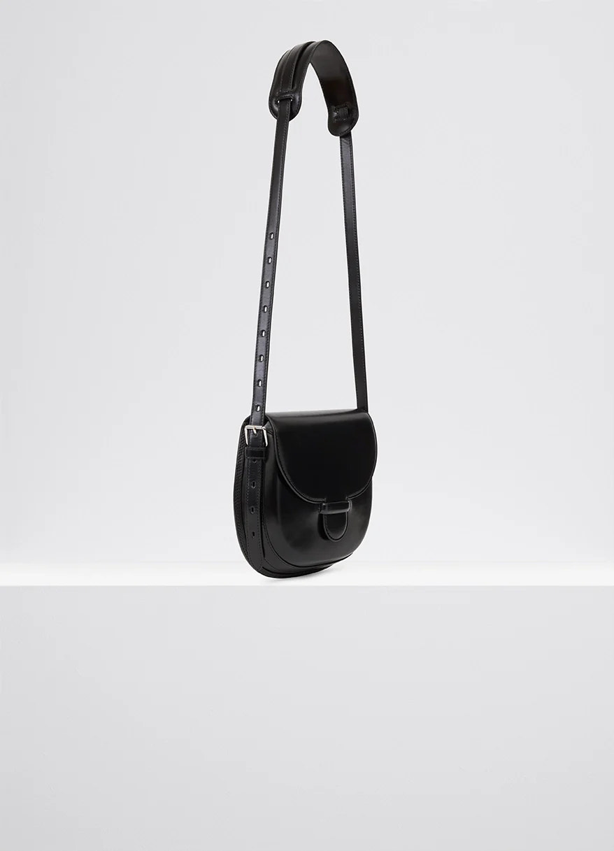 Lemaire cartridge sport bag in black vegetable-tanned leather, product shot, angled top-down view adjustable strap detail
