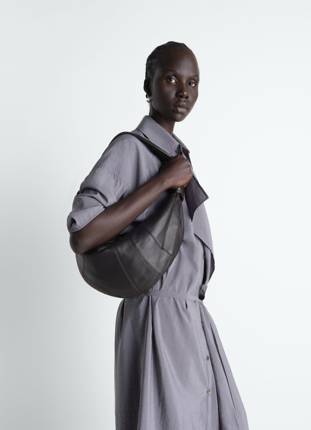 Fortune Croissant leather bag in dark brown worn by model with grey dress side view LEMAIRE