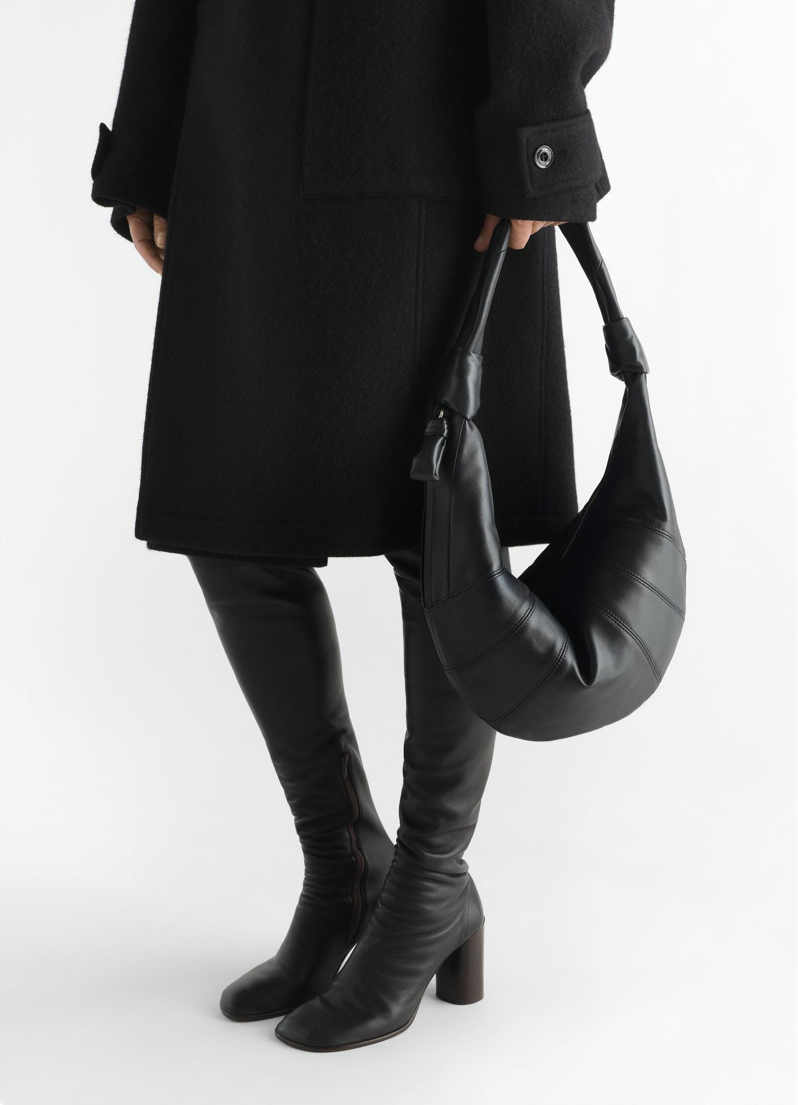 Fortune croissant black leather bag by lemaire held by model in black coat and boots front view