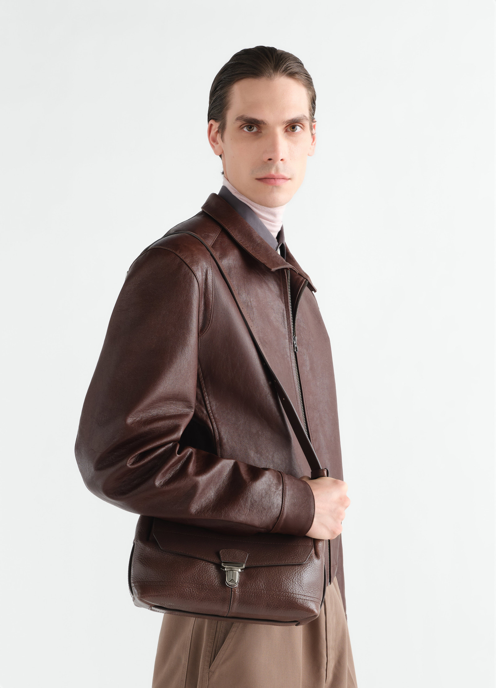 Small brown leather gear bag lemaire worn by model side view with leather jacket and beige pants