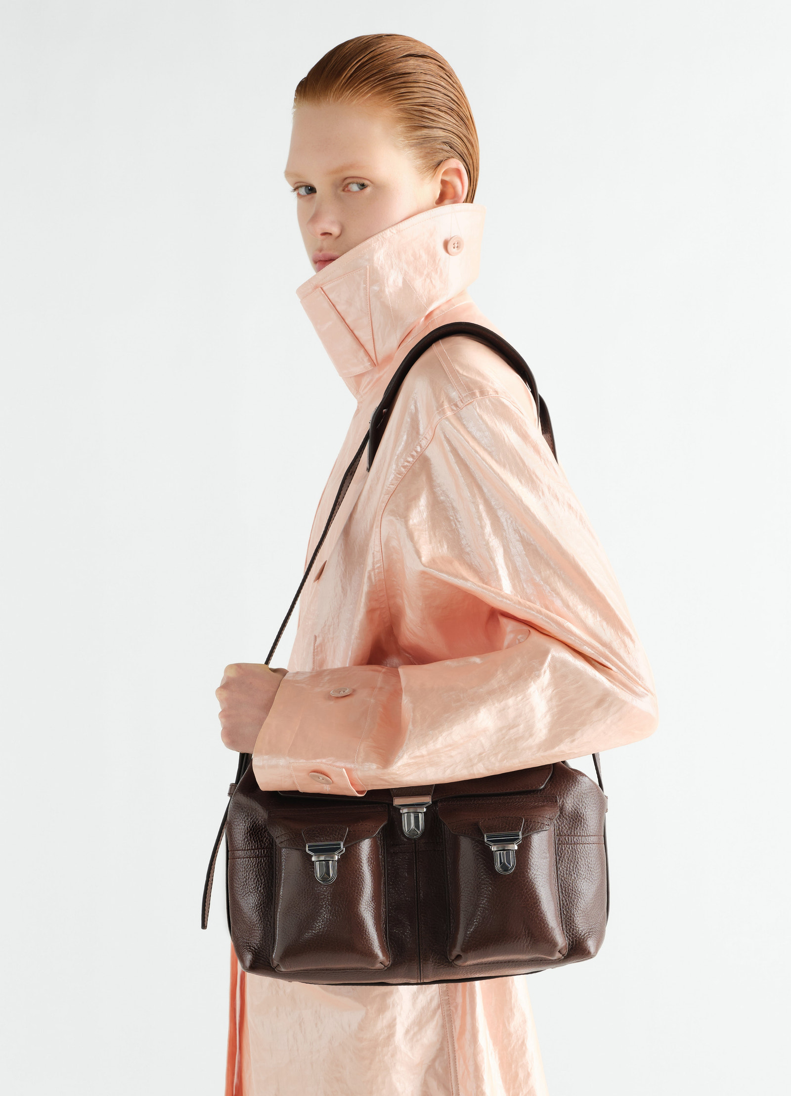 Medium brown leather gear bag by lemaire worn by model seen from side with high collar coat