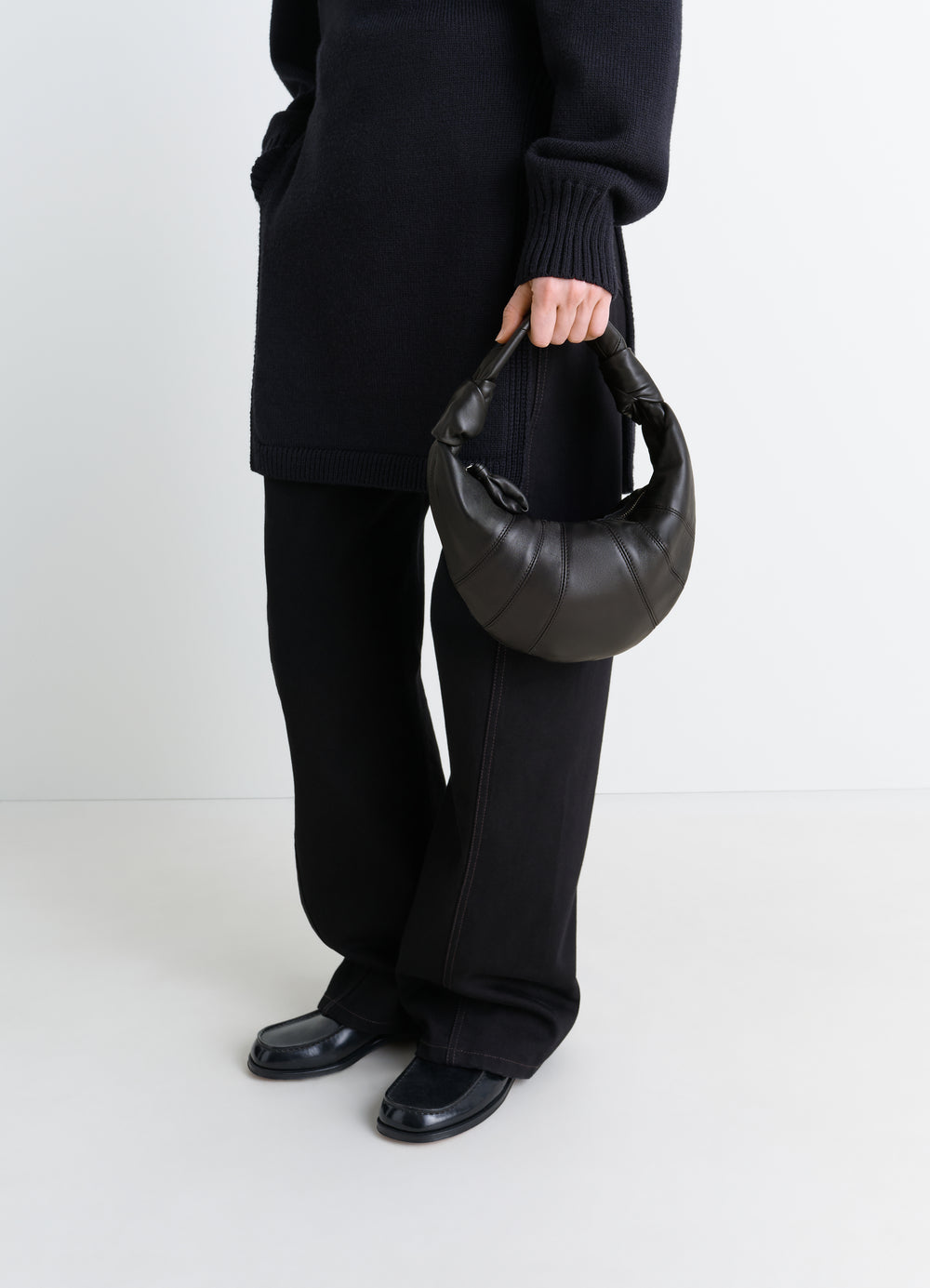 Mini Fortune Croissant bag in black leather by LEMAIRE worn by model with black outfit front view