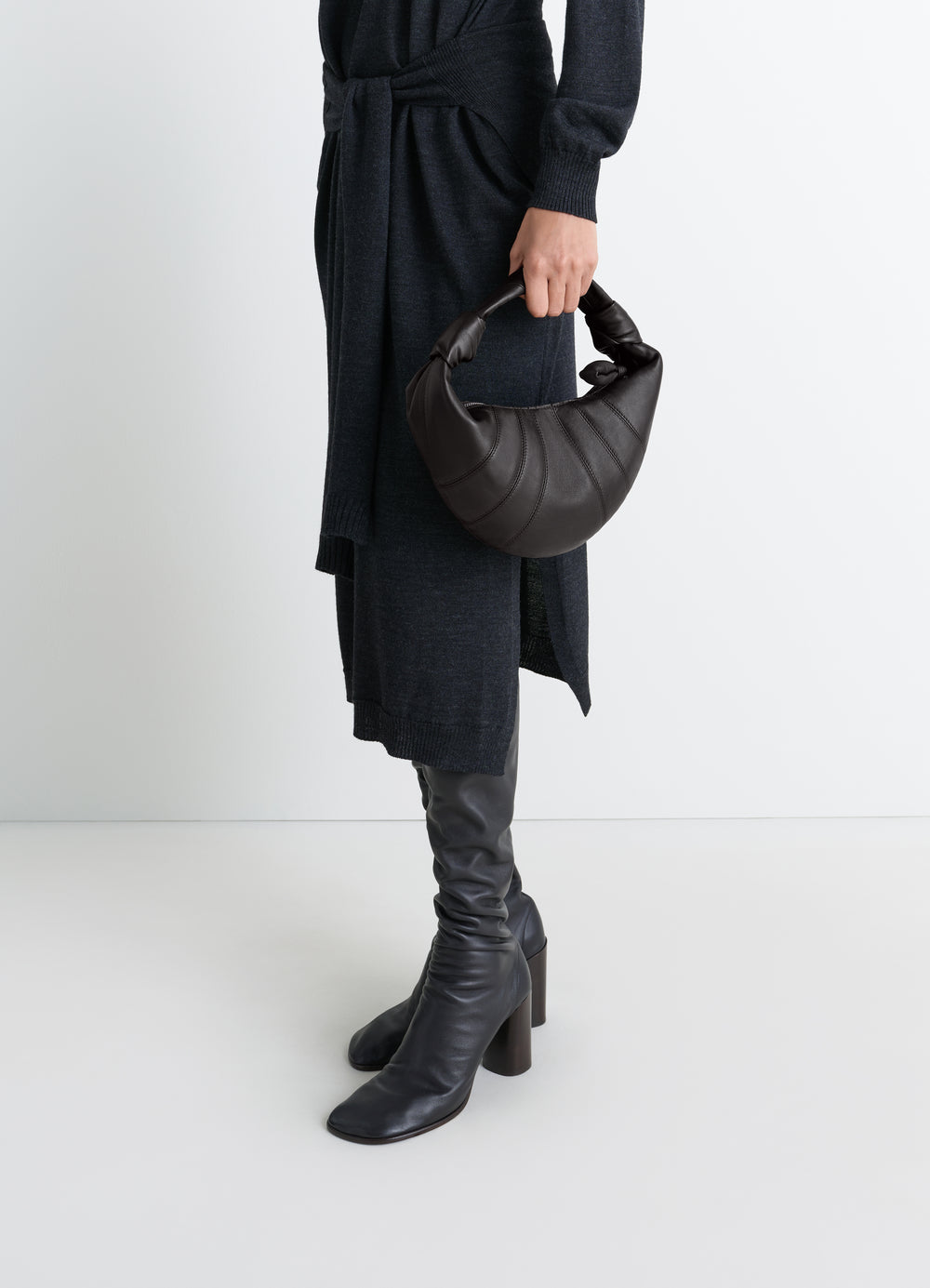 Mini Fortune Croissant leather bag in dark brown by LEMAIRE, worn by model with black knit dress and boots side view