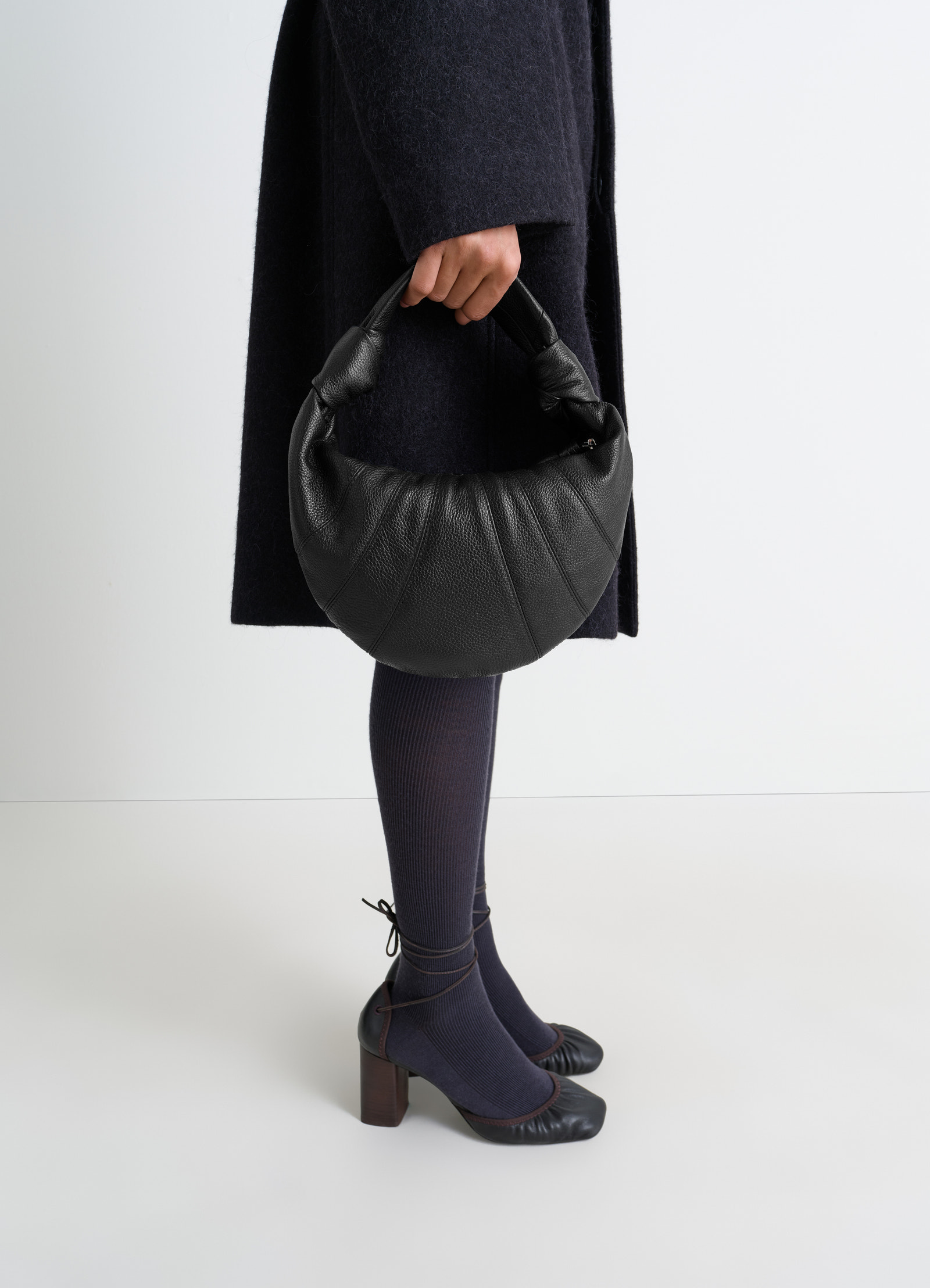 Mini fortune croissant bag in black leather by lemaire worn by model holding handle close-up side view