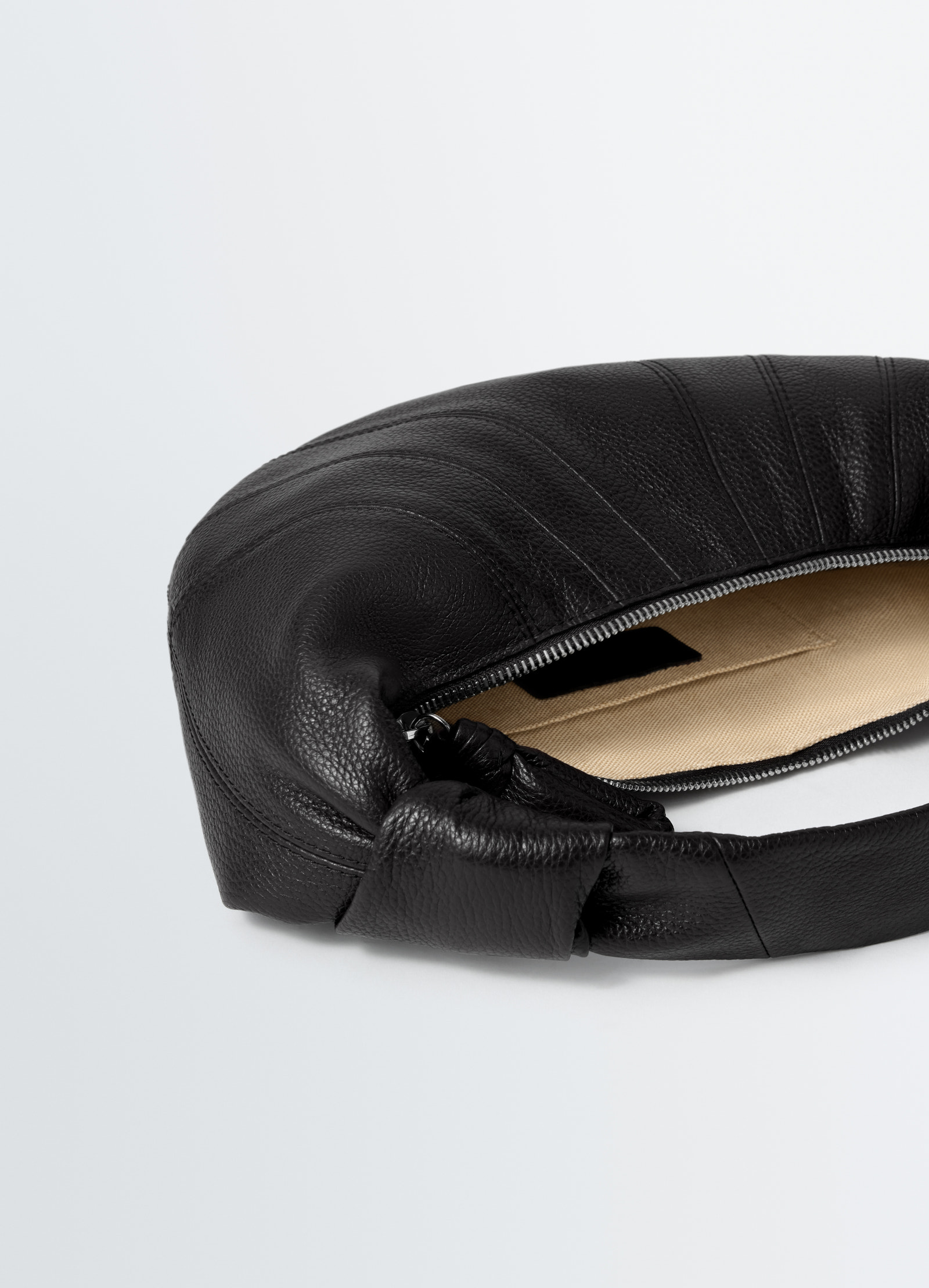 Mini fortune croissant bag lemaire black pebbled leather with open zipper showing beige fabric lining on white background