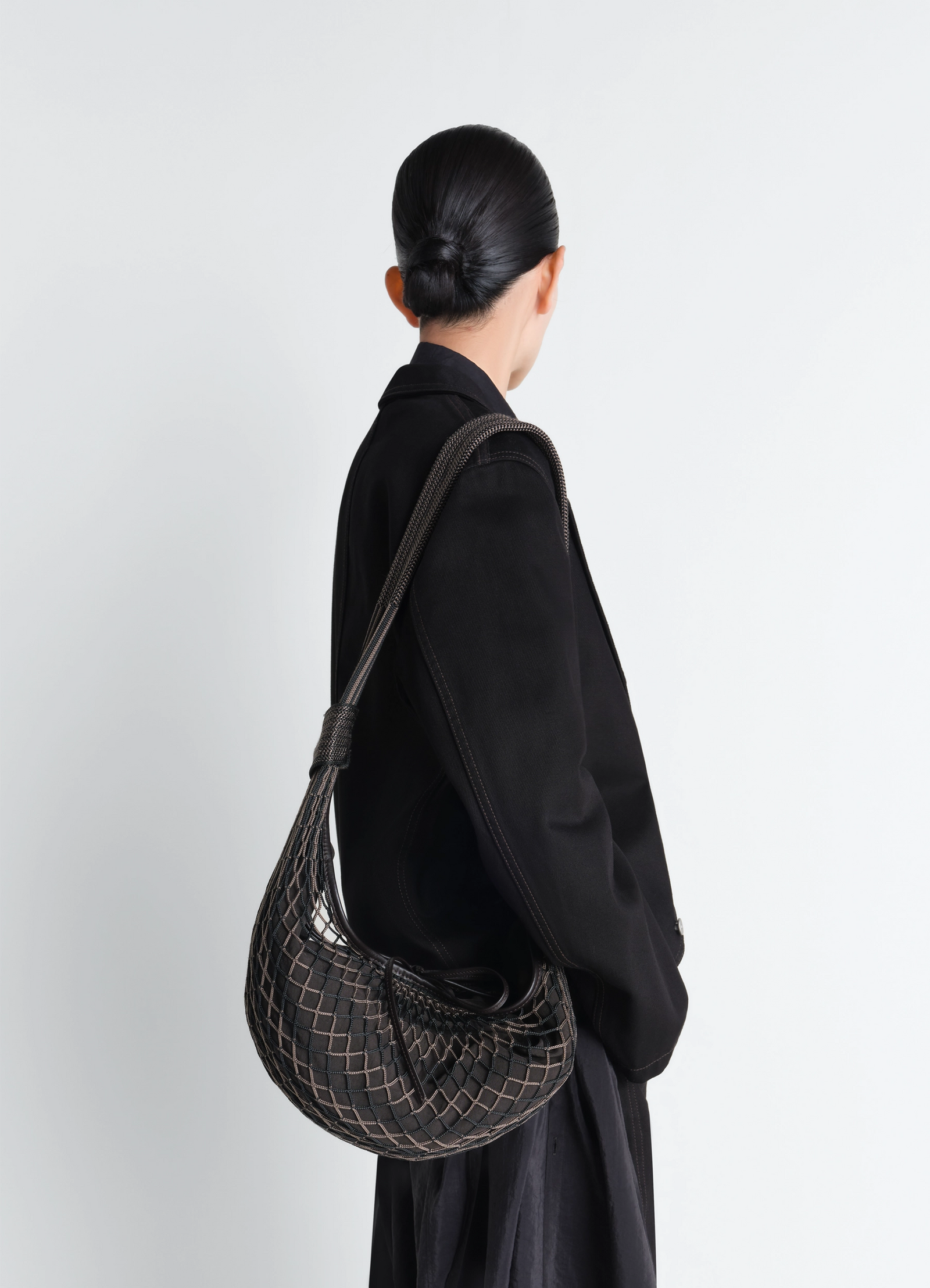 Lemaire croissant filt bag in black nylon net, model shot, back view worn over shoulder