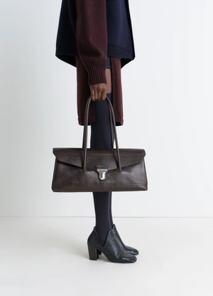 Lemaire Shoulder Gear Bag in Dark Brown Vegetable-Tanned Leather, model shot, Side view Flap closure with metal clip