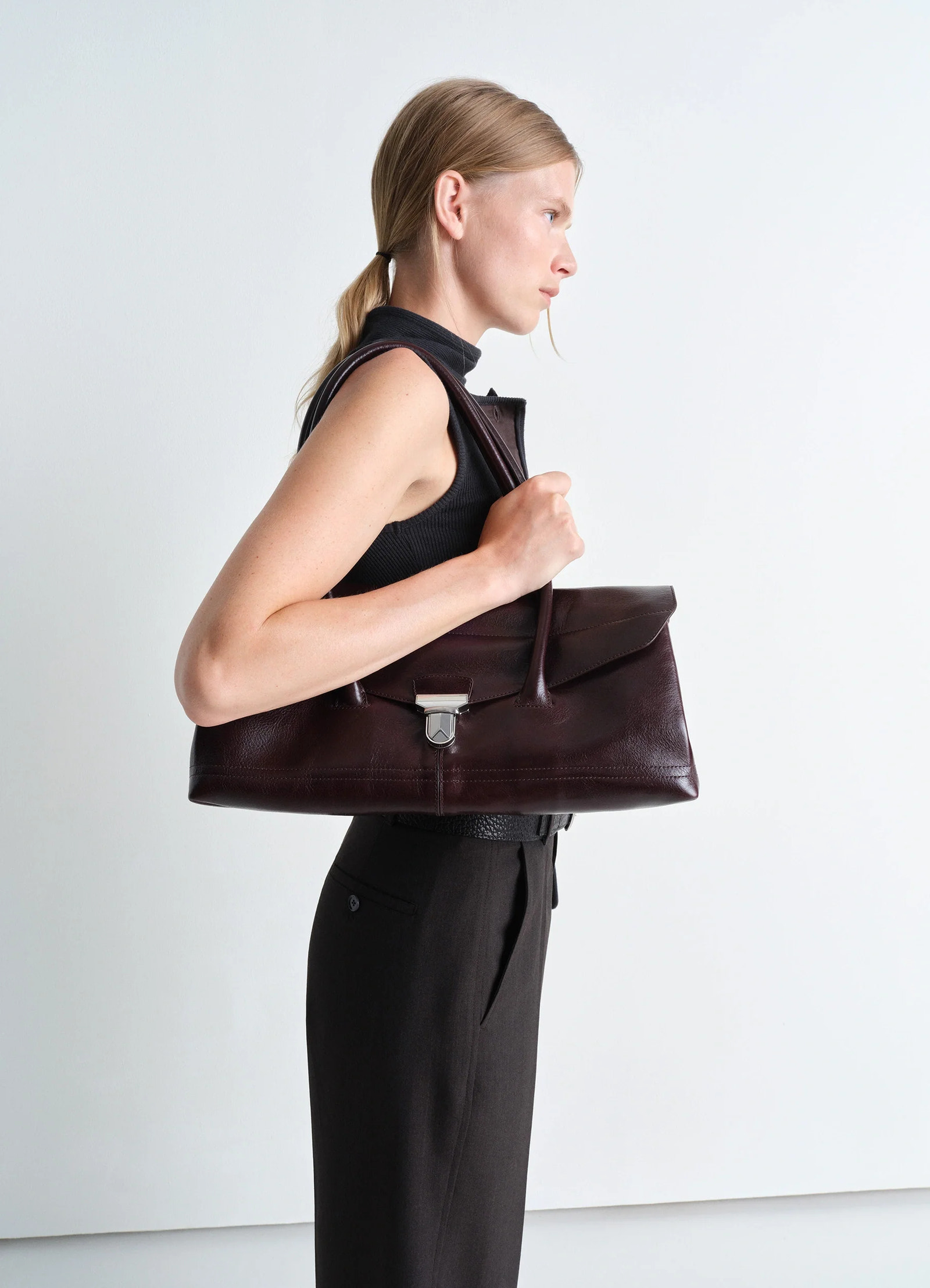 Lemaire shoulder gear bag in glossy vegetable-tanned leather, model shot, side view metal clip clasp detail