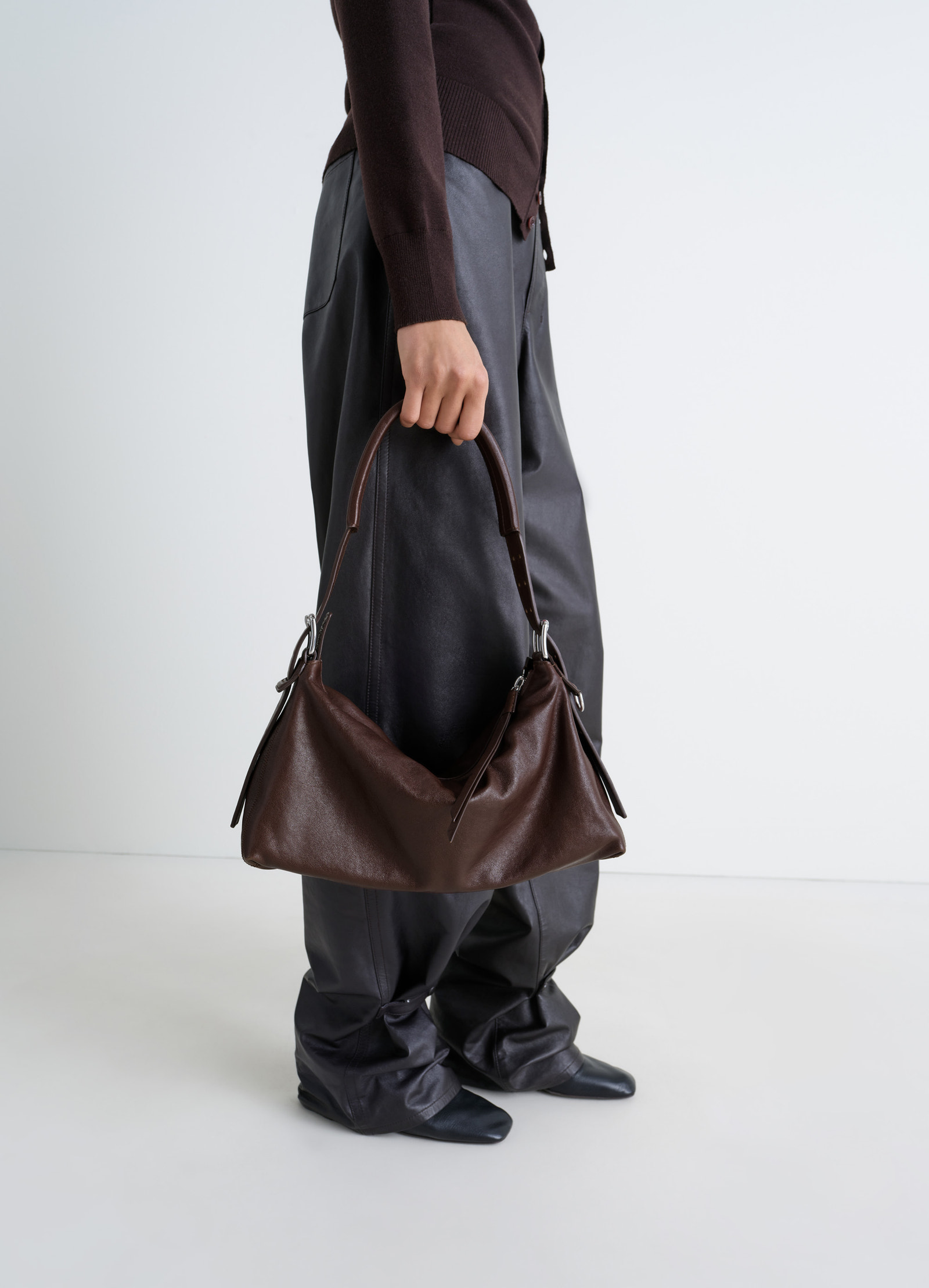 Belted baguette bag in brown paper lux leather, model shot, held by model side view slouchy leather texture