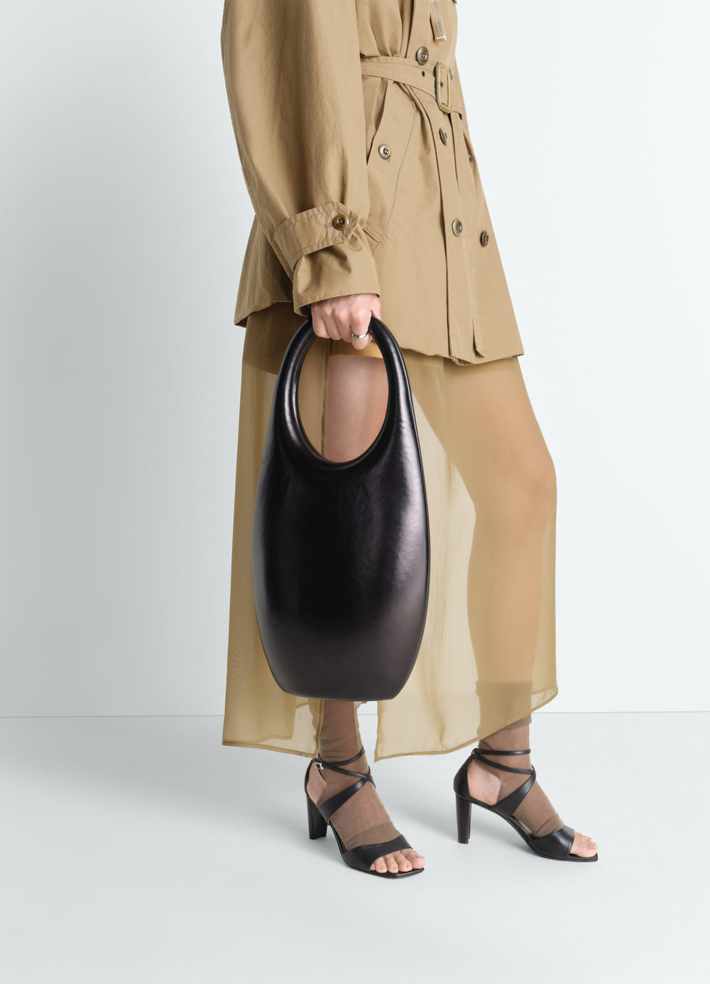 Carlos Peñafiel Naho black leather bag worn by model with beige trench coat and sheer skirt LEMAIRE