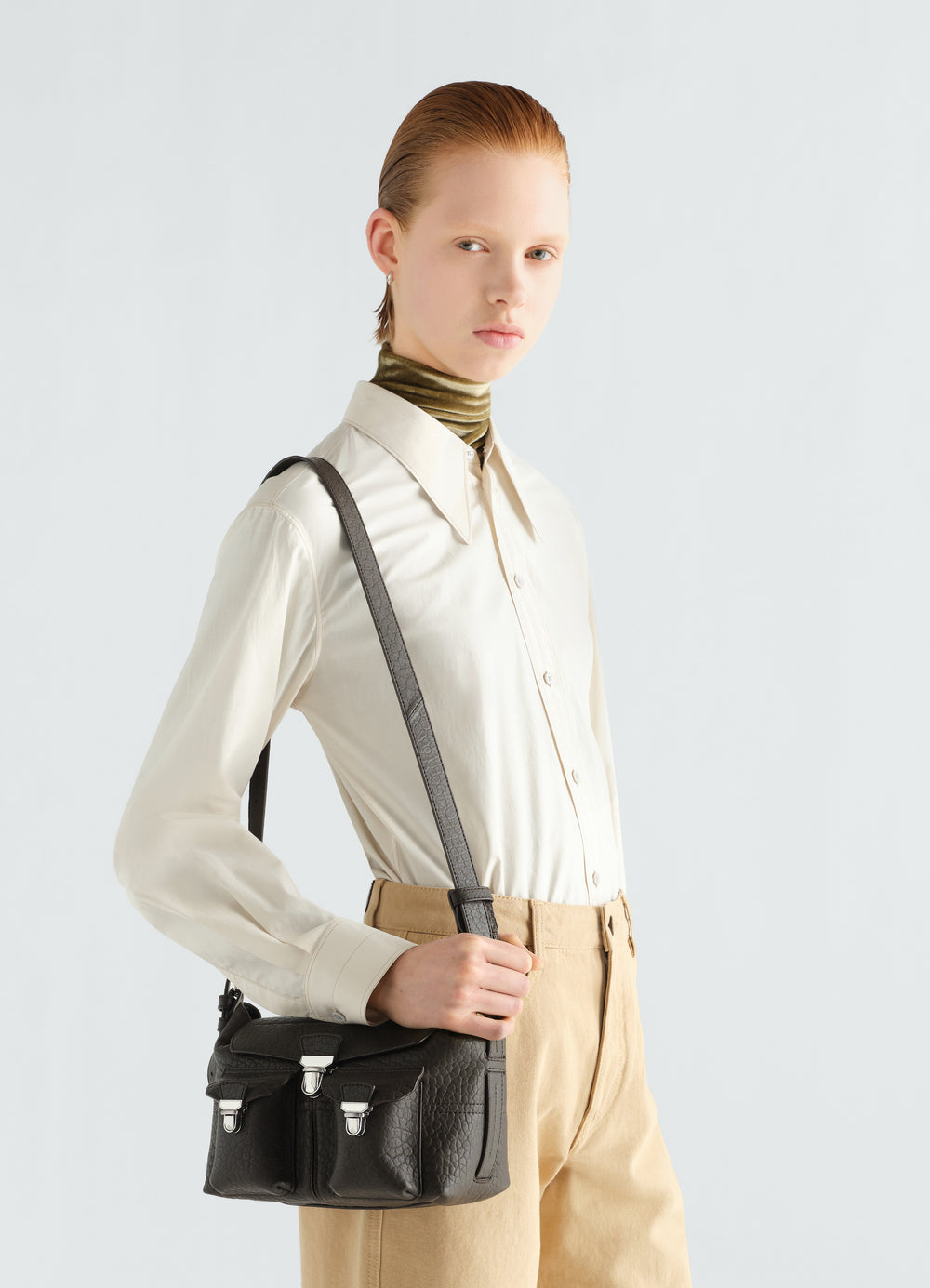 Mini Soft Gear Bag in black bubble lambskin by LEMAIRE worn by model with cream shirt and beige pants side view