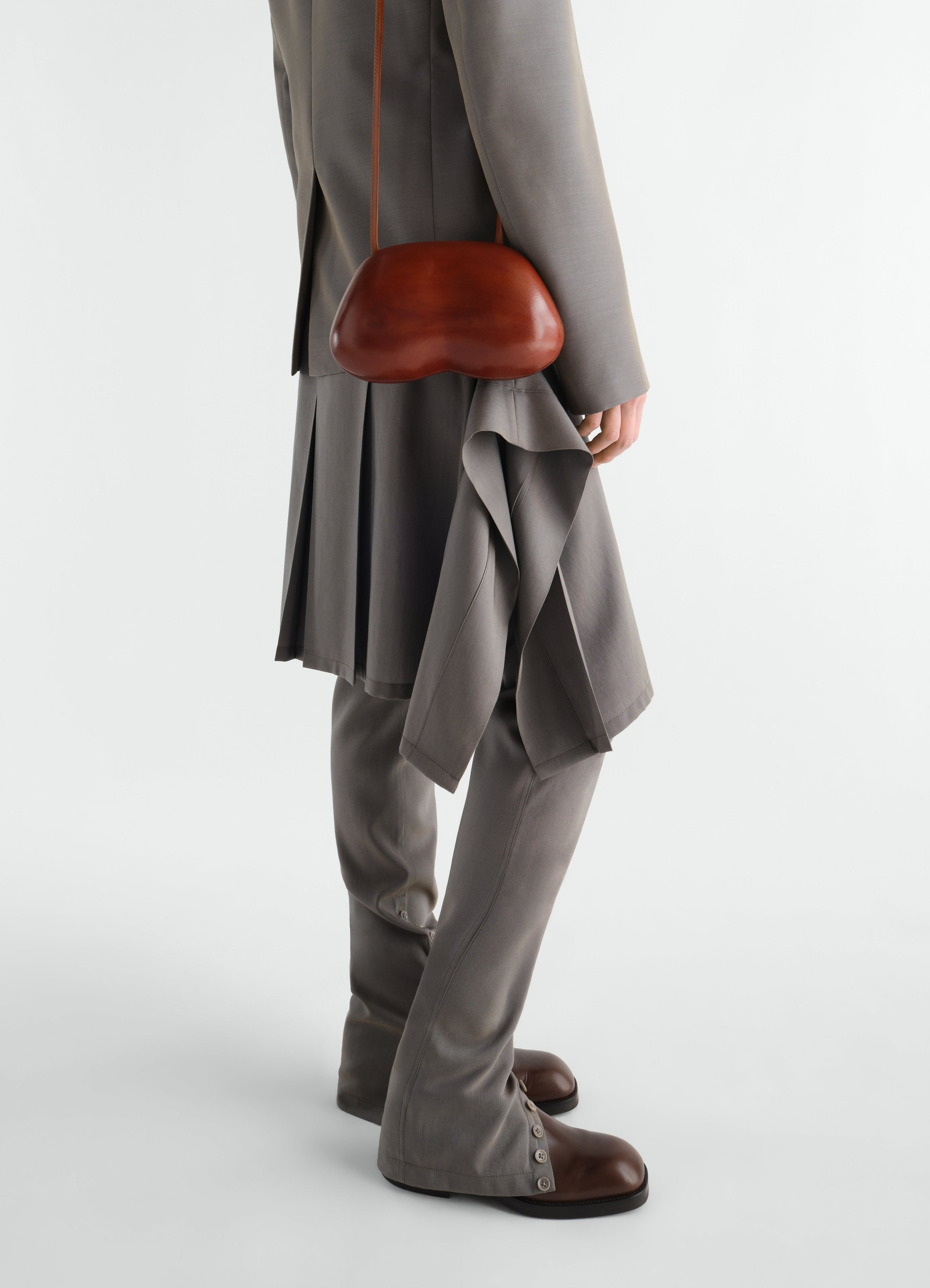 Fesses clutch in brown patinated calfskin lemaire worn by model side view with grey layered outfit and matching trousers