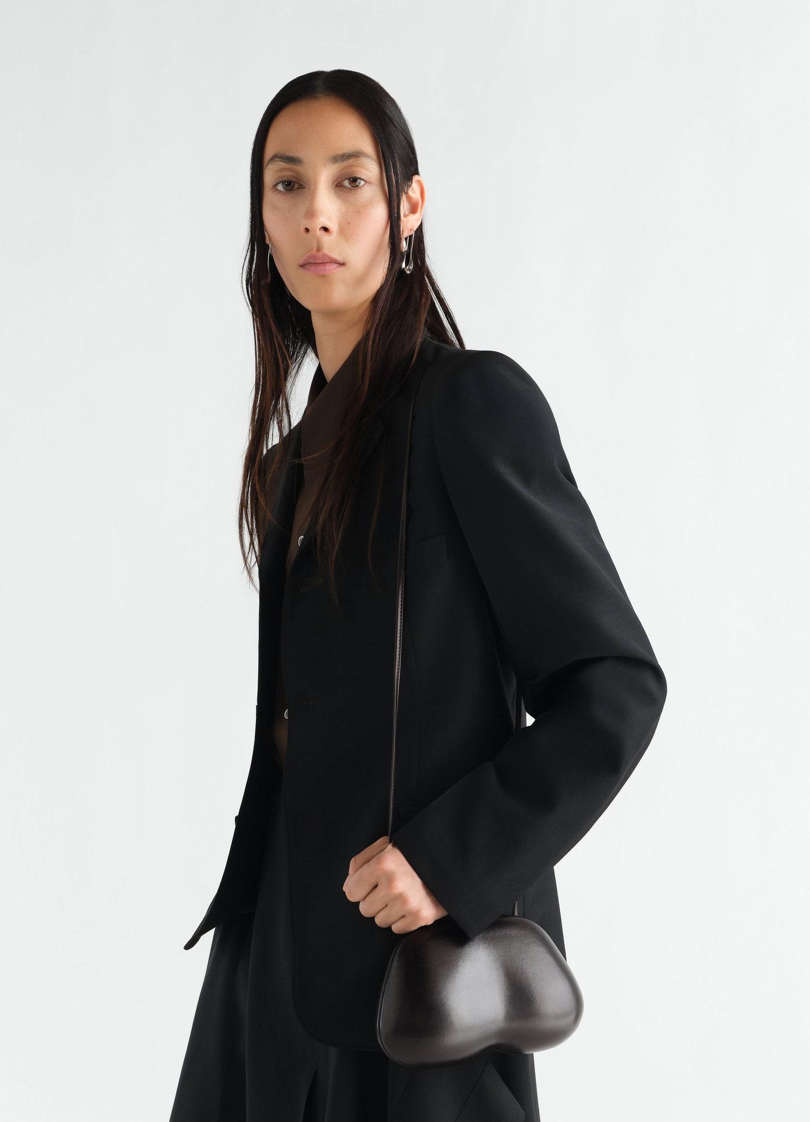 Fesses clutch in black patinated calfskin by lemaire worn by a model with black blazer side view