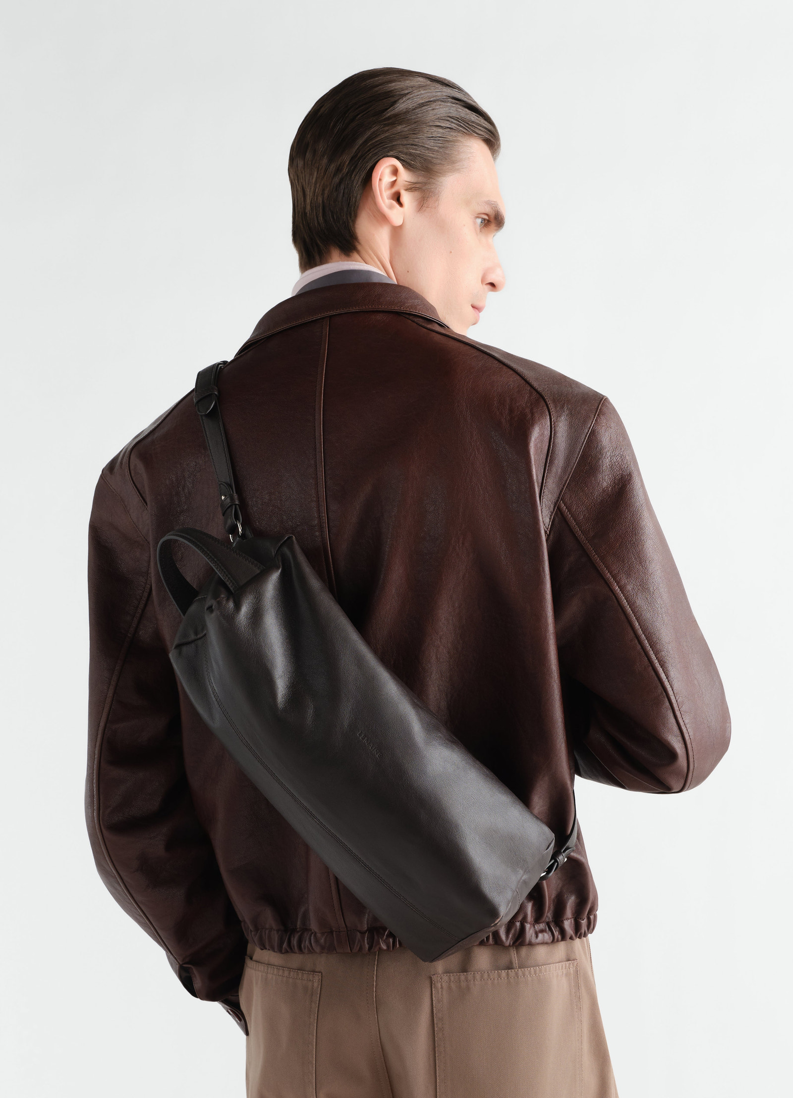 Care shoulder bag lemaire in black nappa lambskin worn by model back view with brown leather jacket