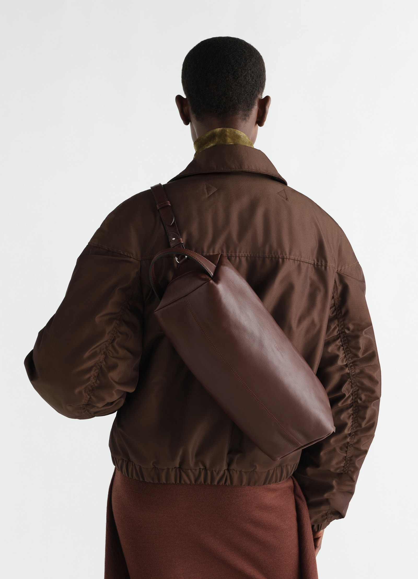 Care shoulder bag in brown nappa lambskin lemaire worn by model back view with brown jacket