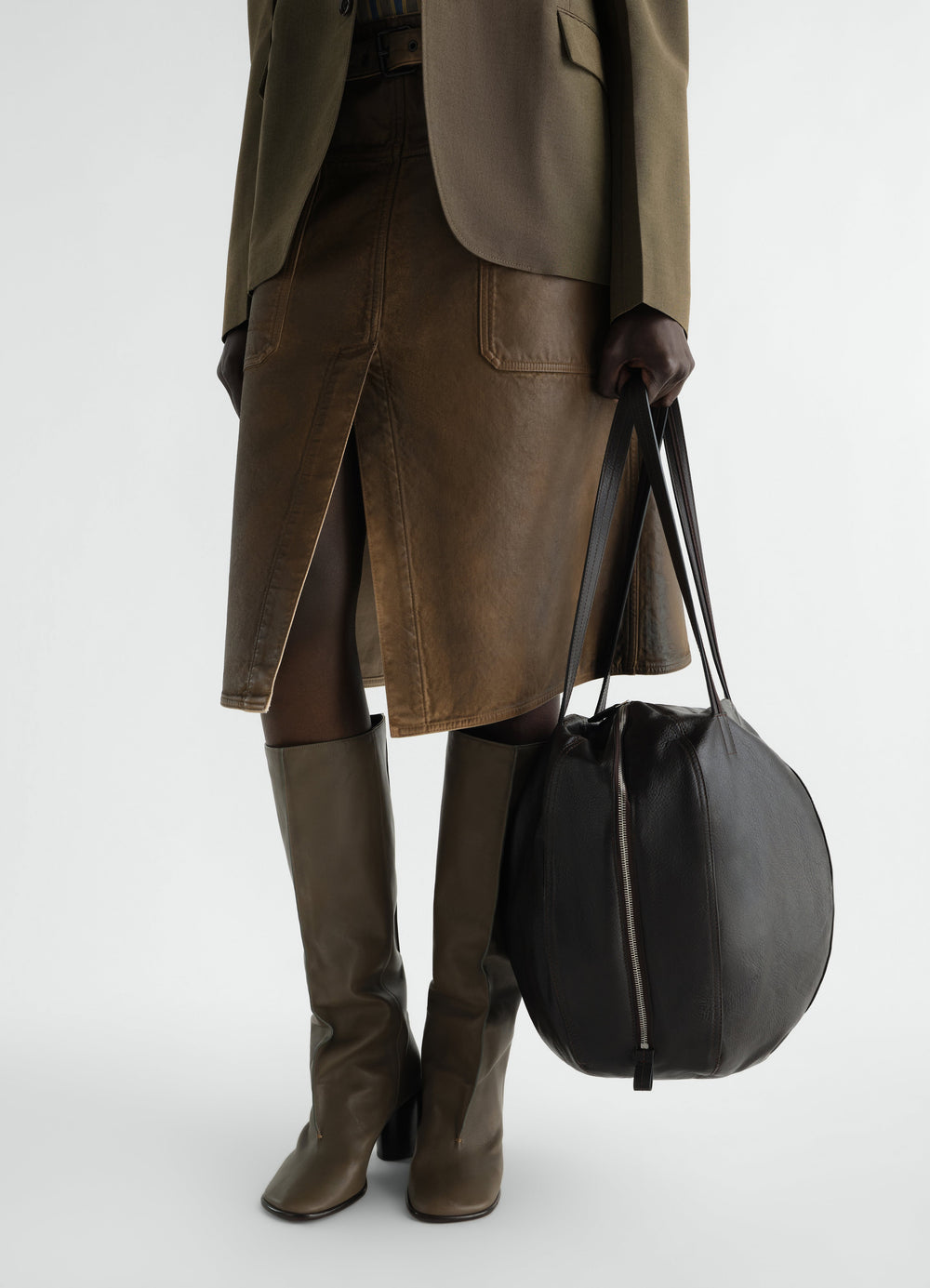 Hobo helmet bag in black grained leather LEMAIRE worn by model with brown leather skirt and green boots front view