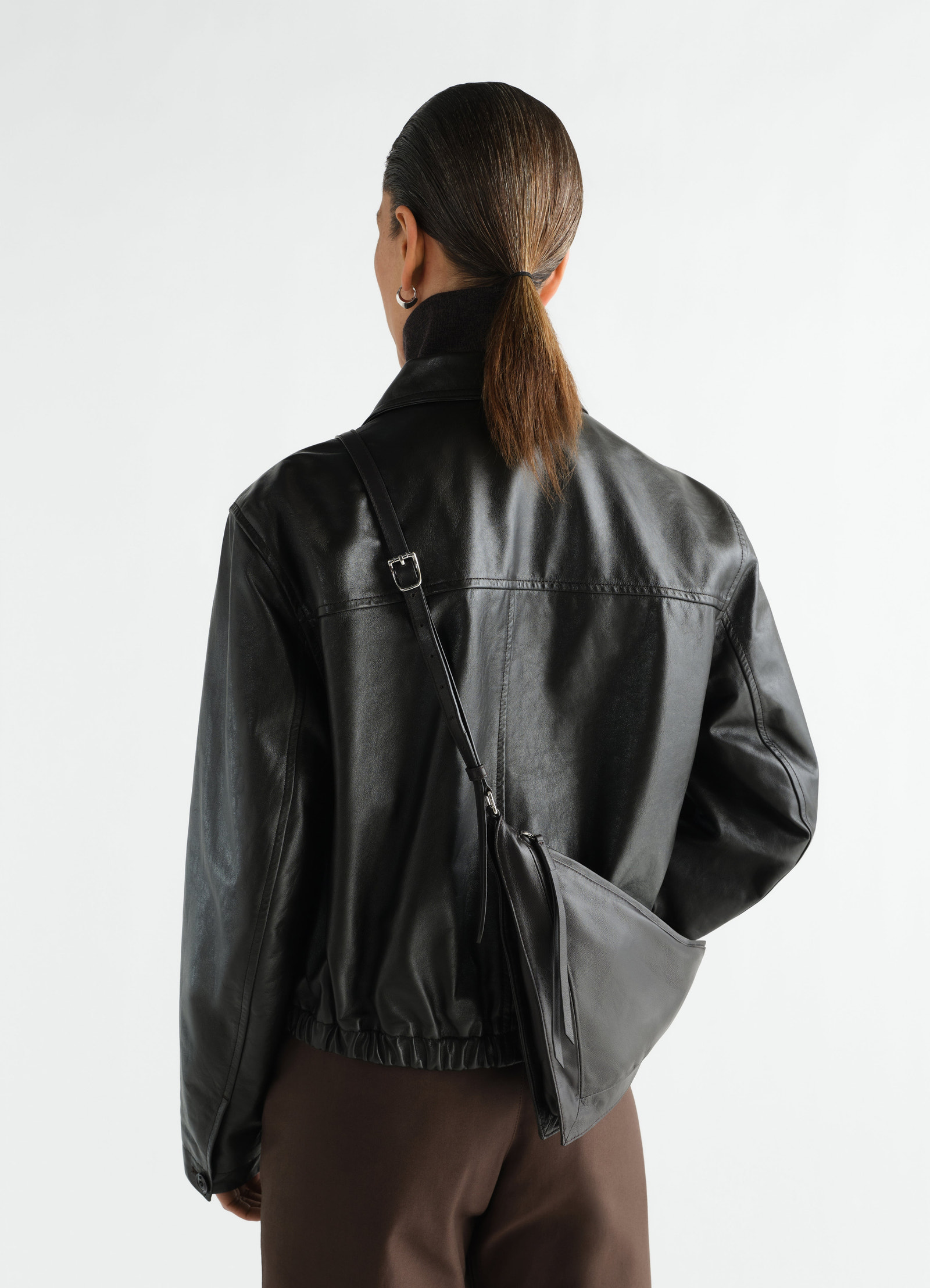 Pocket scarf bag in shiny black nappa lambskin by lemaire worn by model back view with jacket