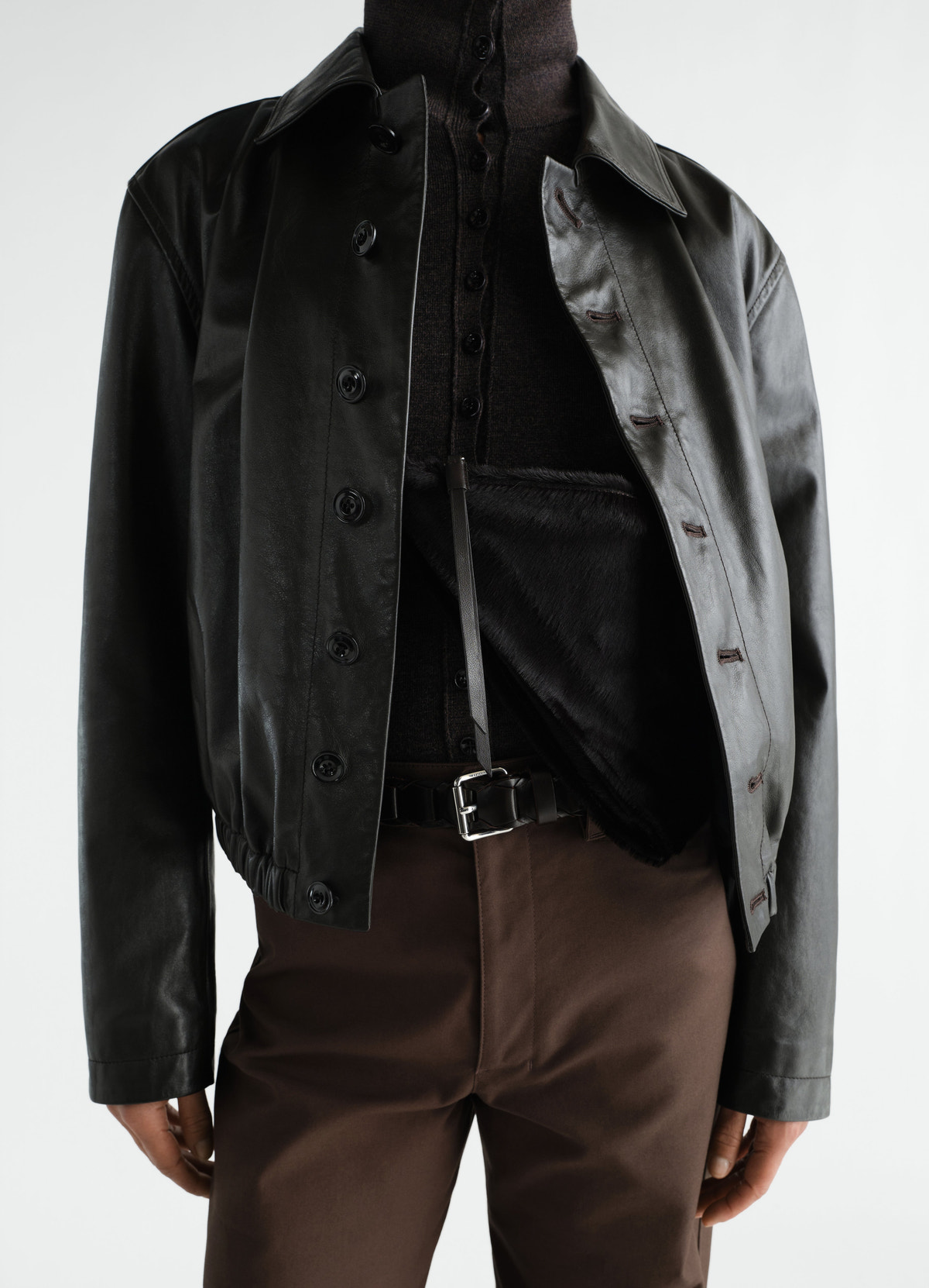 Pocket scarf bag in black pony-style leather with strap, worn with black leather jacket and brown pants, lemaire