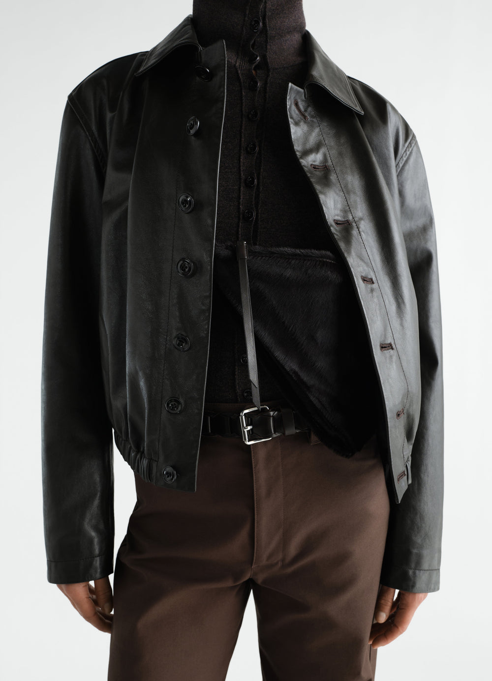 Pocket scarf bag in black pony-style leather with strap, worn with black leather jacket and brown pants, LEMAIRE