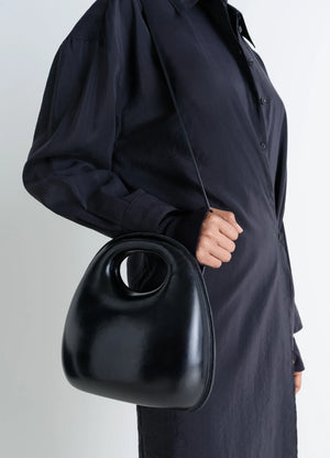 Lemaire Egg Bag in Black Patinated Leather, model shot, side view cross-body carry