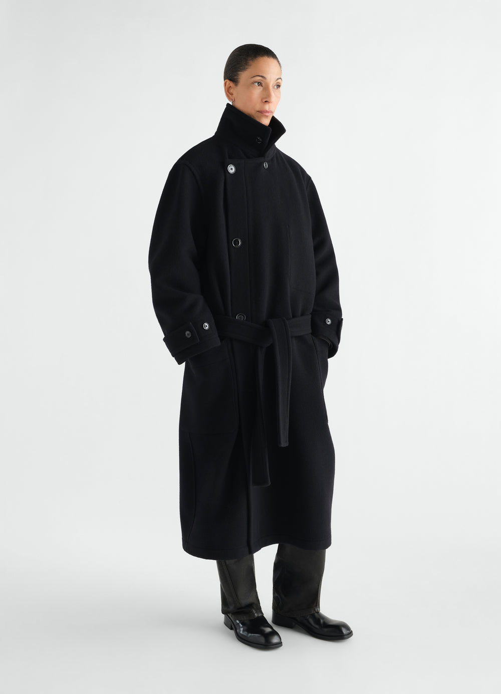 Wrap coat in black wool with high collar and belt worn by model LEMAIRE front view