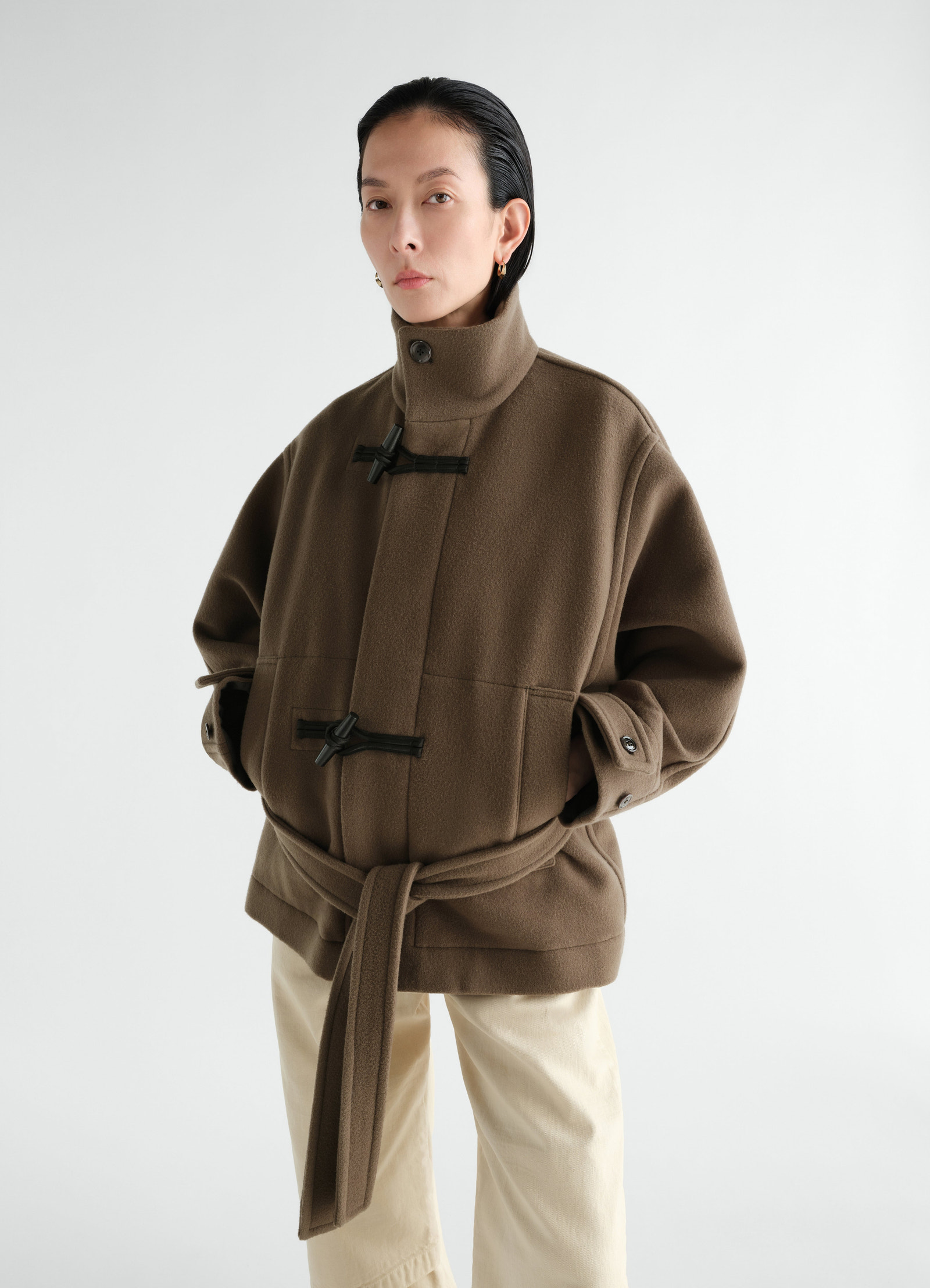 Short brown wool duffle coat with black toggles and belt worn by model lemaire front view