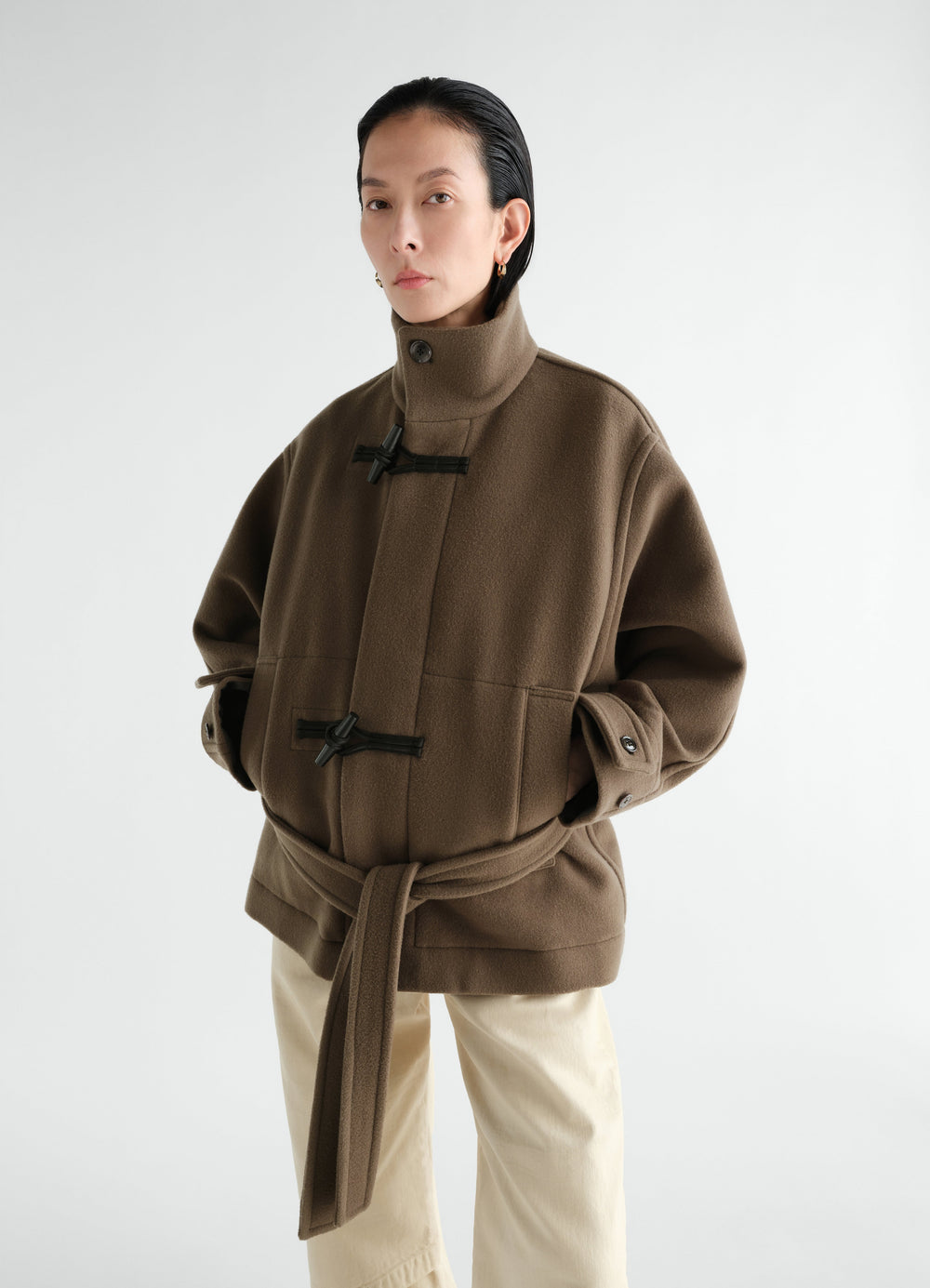 Short brown wool duffle coat with black toggles and belt worn by model LEMAIRE front view
