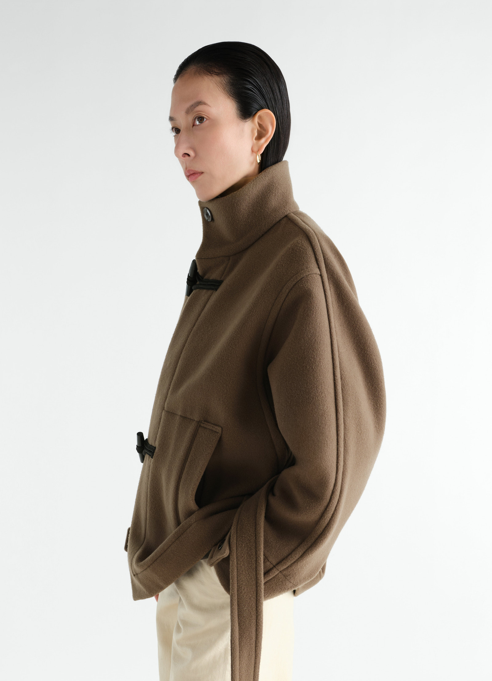 Short brown wool duffle coat with high collar and toggle closures worn by model lemaire side view