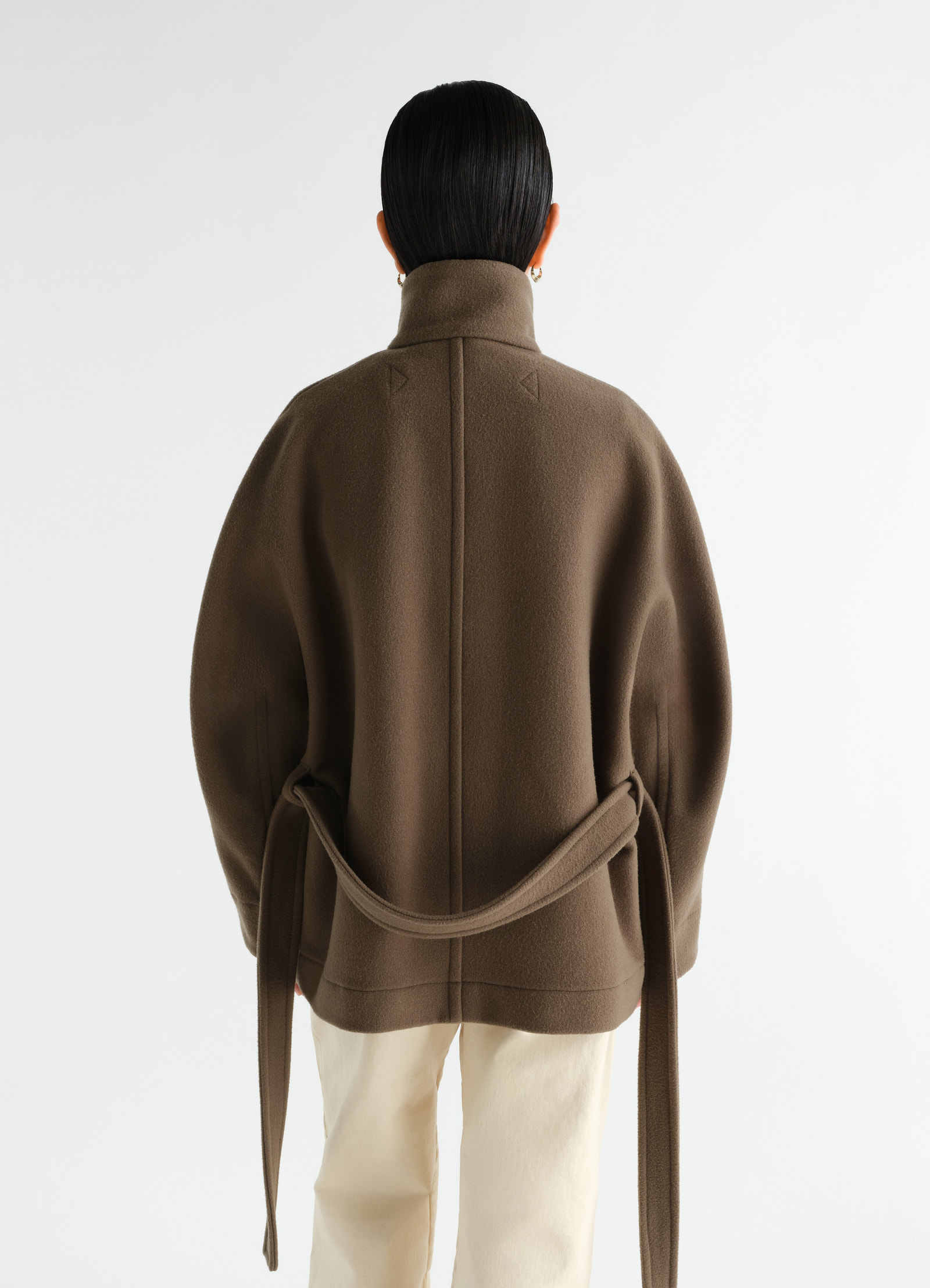 Short brown wool duffle coat by lemaire worn by a model, back view with loose belt and high collar.