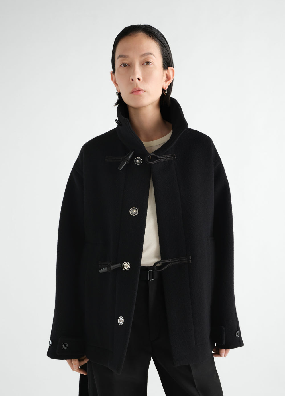 Short black wool duffle coat with toggle buttons worn by a model front view LEMAIRE
