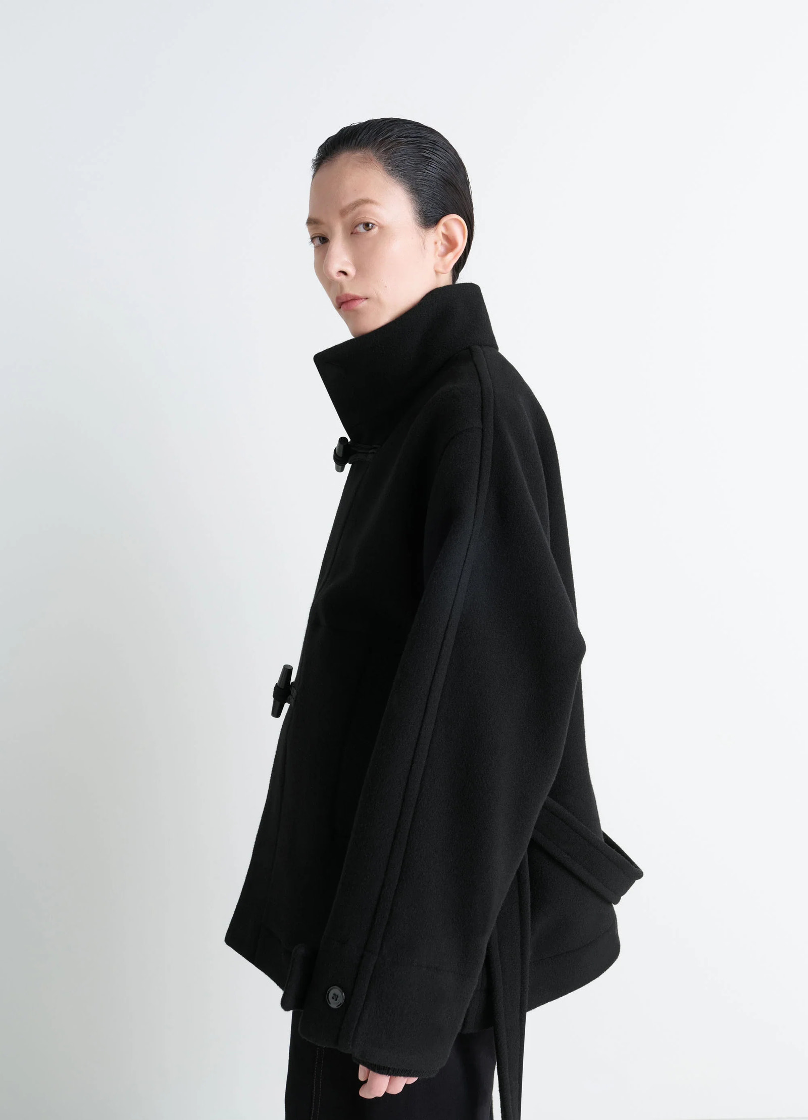 Lemaire short duffle coat in black double-faced wool, model shot, three-quarter side view high collar, side button detail