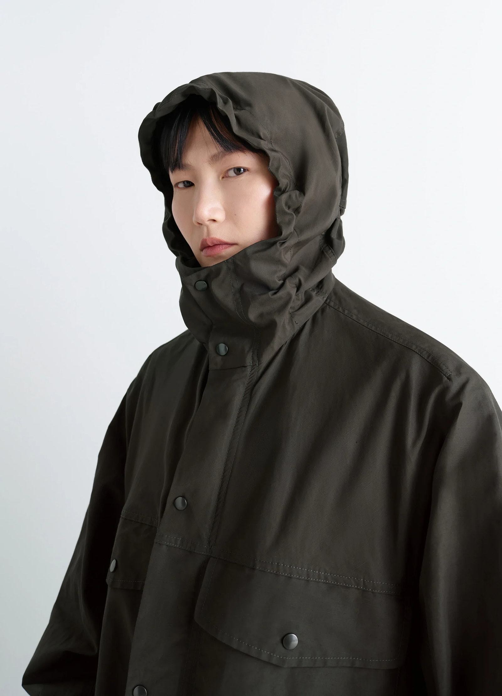 Lemaire utility raincoat in khaki linen cotton blend, model shot, close-up hooded view hooded design, protective flaps