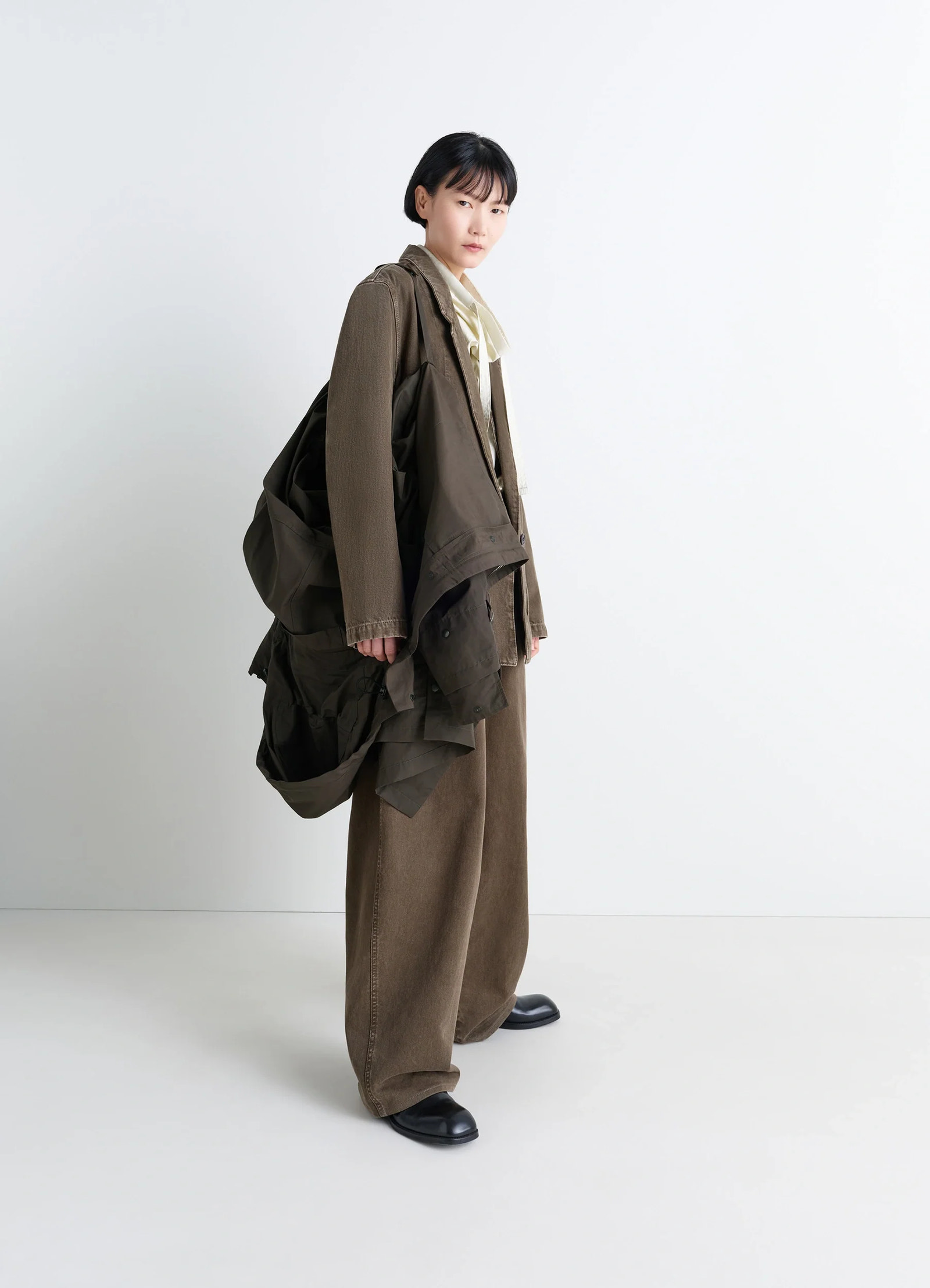 Lemaire utility raincoat in khaki linen cotton blend, model shot, back three-quarter view draped over shoulder